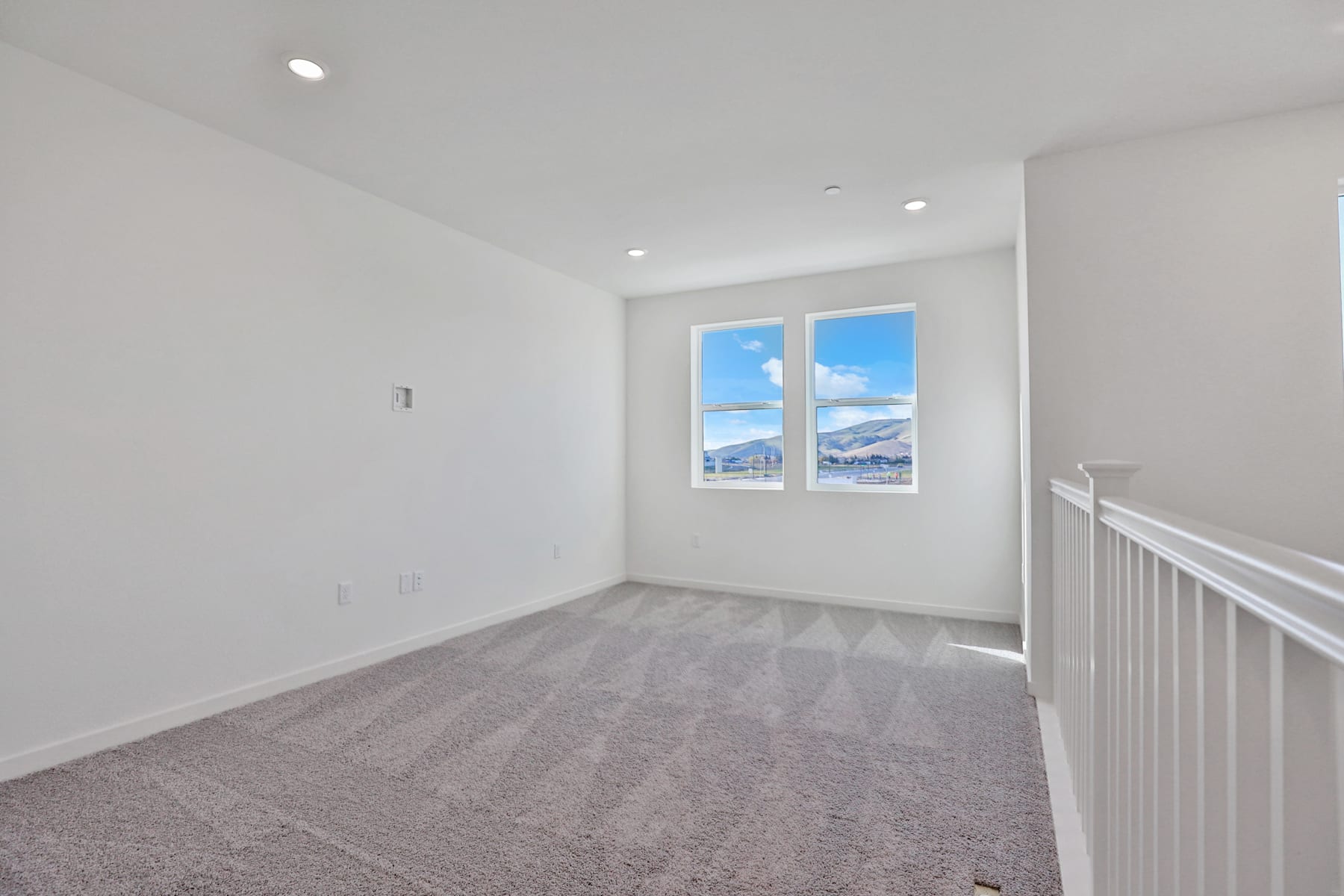 A bright, spacious room with white walls, a carpeted floor, and a window overlooking a snowy outdoor scene.