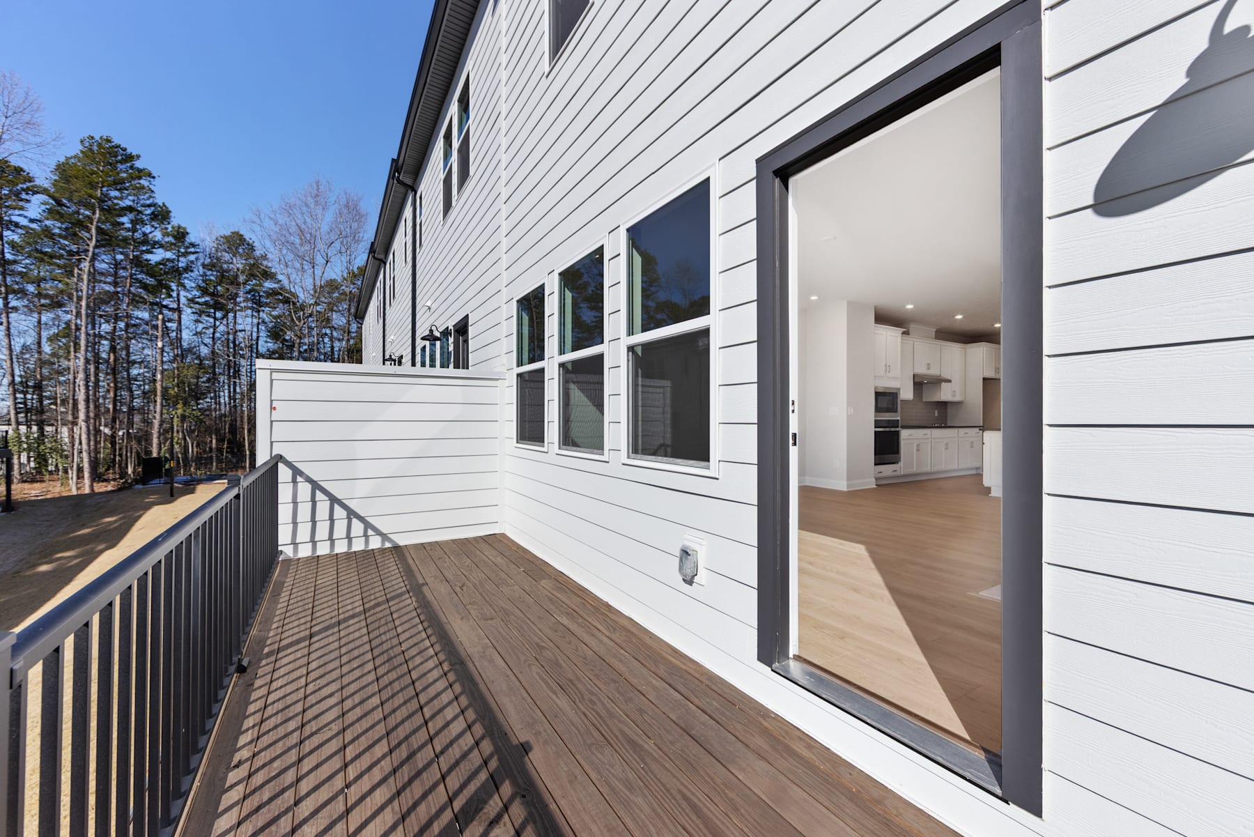 A modern, two-story house with a wooden deck and large windows overlooking a wooded area in the background.