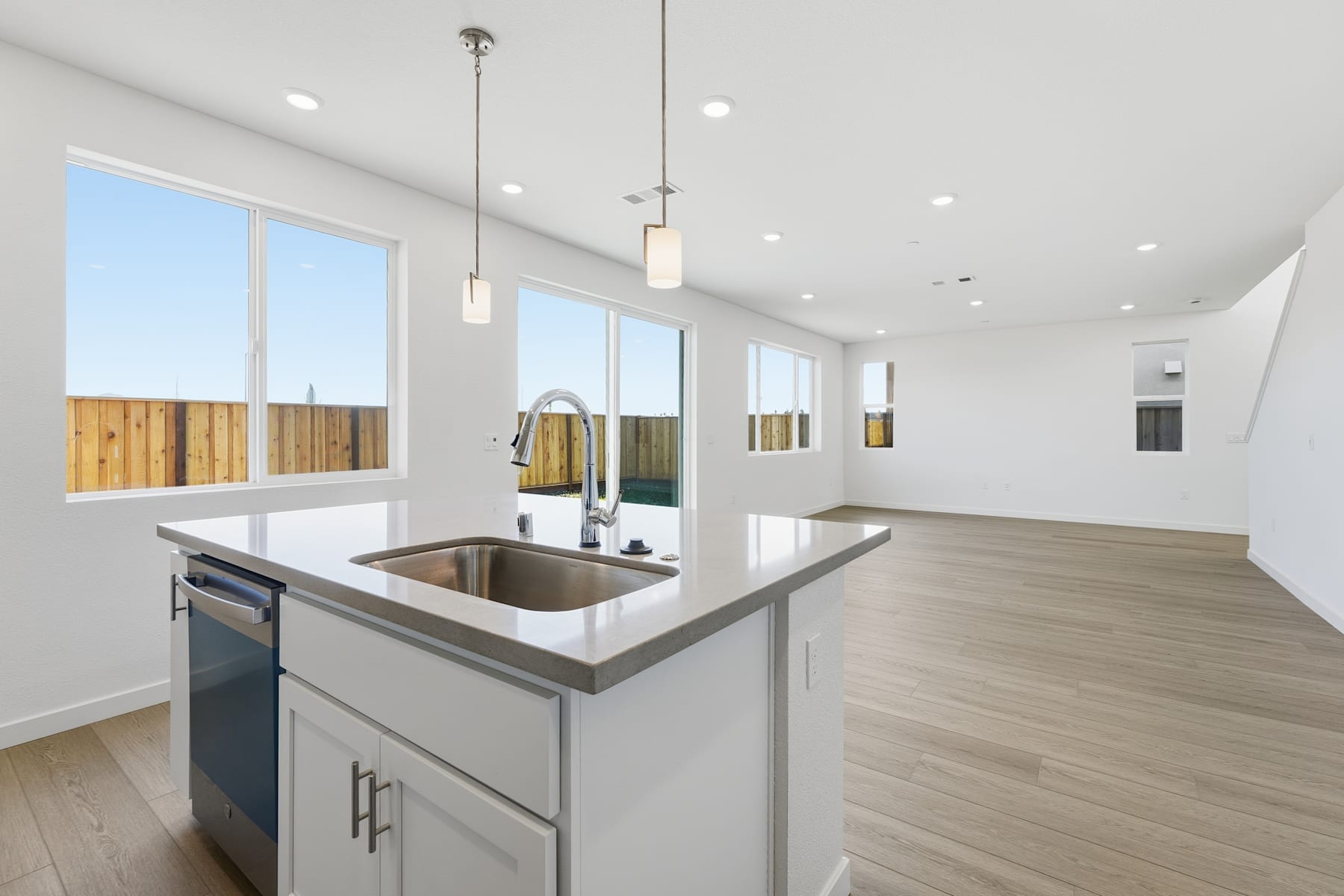 A modern, open-concept kitchen with a stainless steel sink, wooden cabinets, and large windows providing ample natural light.