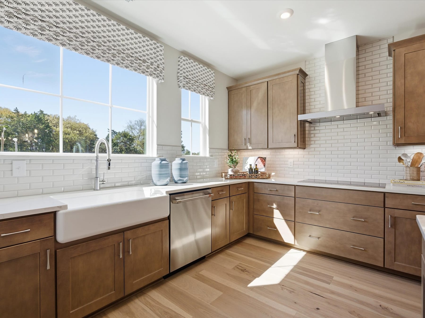 A modern and well-lit kitchen with wooden cabinets, a farmhouse-style sink, and large windows overlooking a scenic outdoor view.