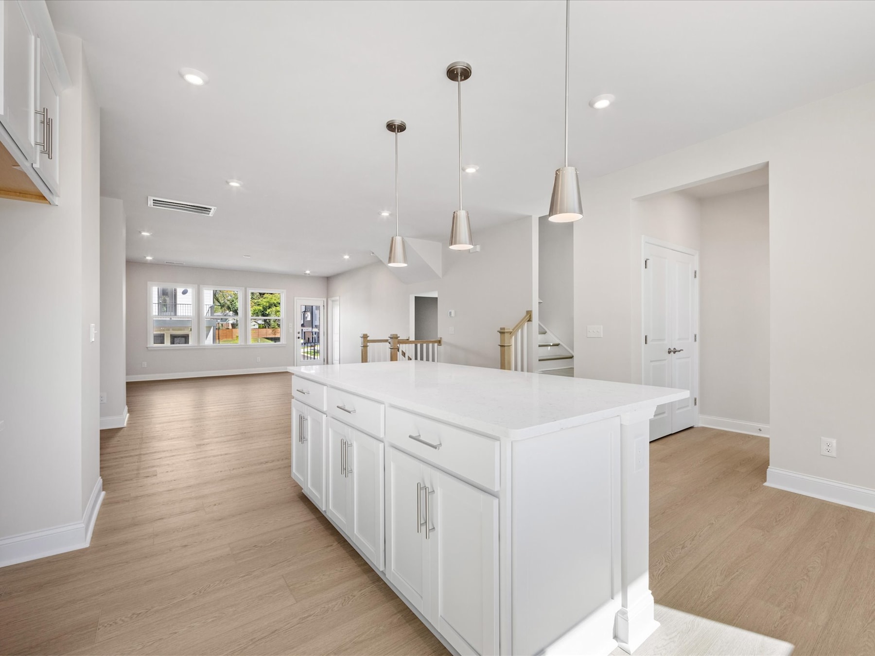 A modern, bright kitchen with white cabinets, a large central island, and pendant lights hanging from the ceiling.