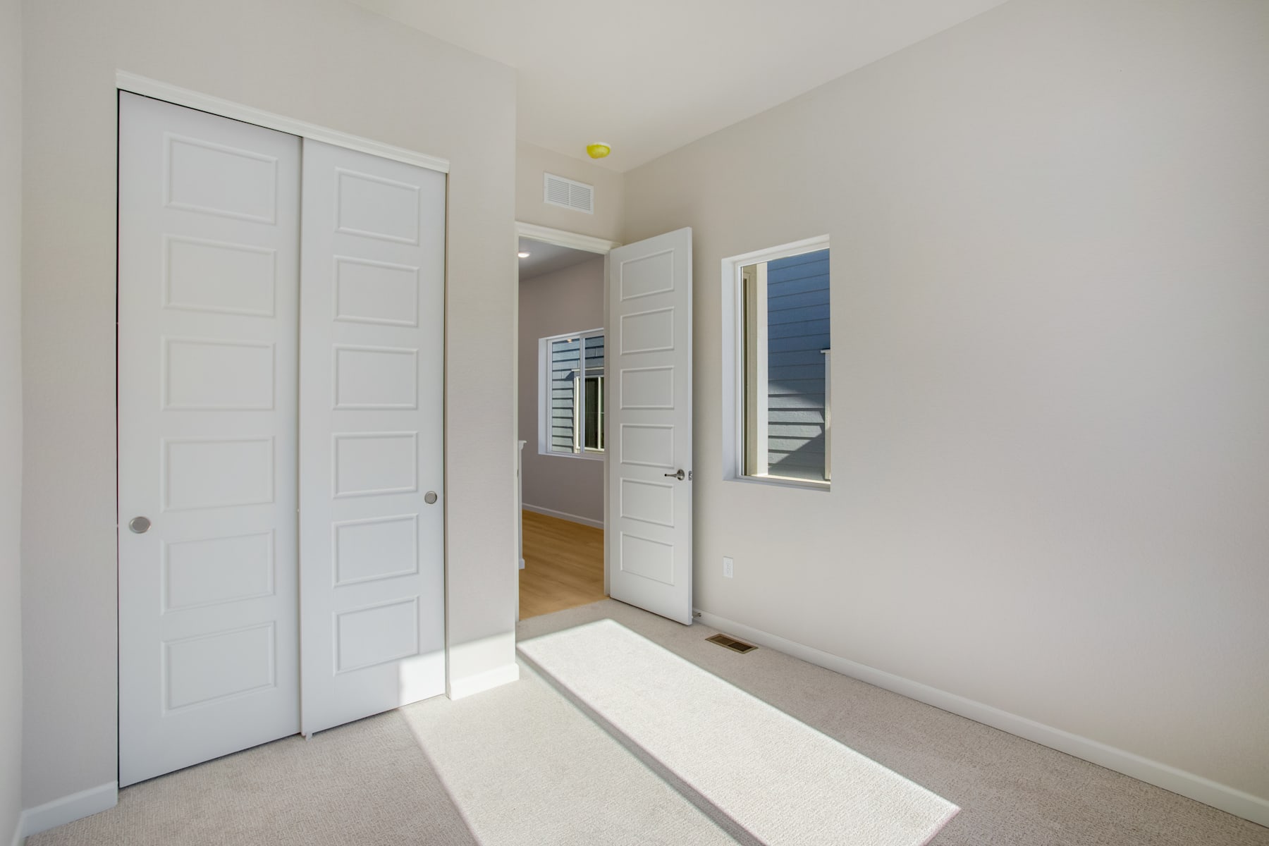 A bright and spacious room with white doors, a mirror, and a light fixture on the ceiling, creating a clean and minimalist atmosphere.