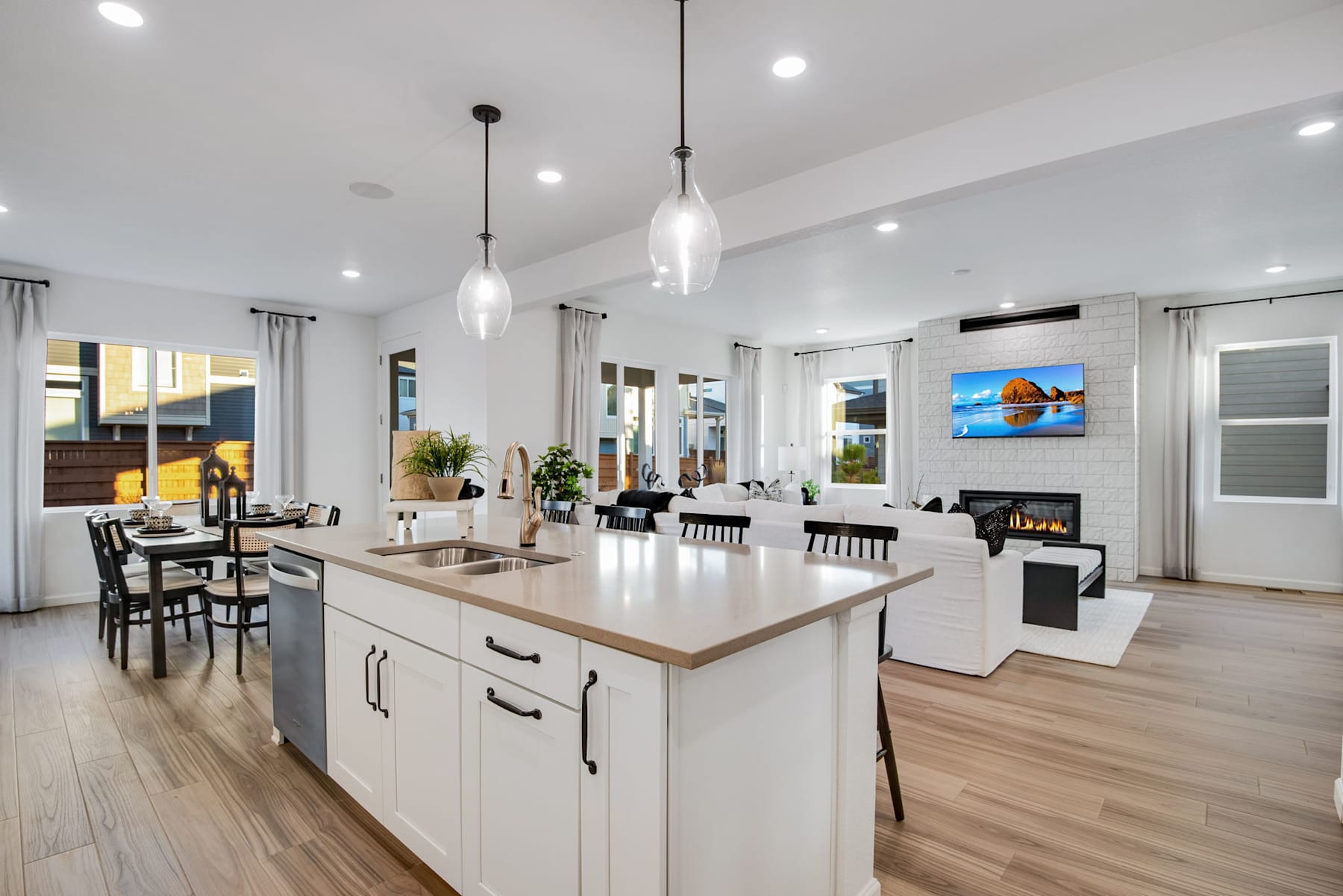 A modern, open-concept kitchen and living room with a large central island, pendant lighting, and a fireplace in the background.