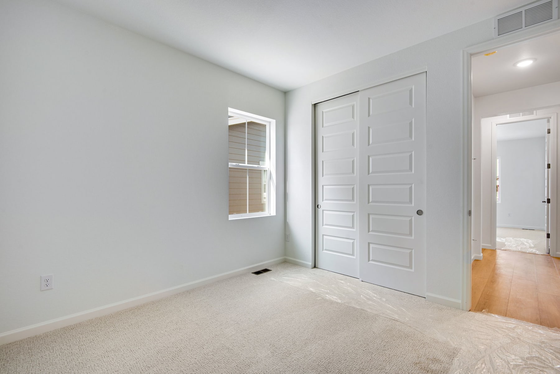 A bright, minimalist room with white walls, a wooden floor, and a large white door leading to another room.