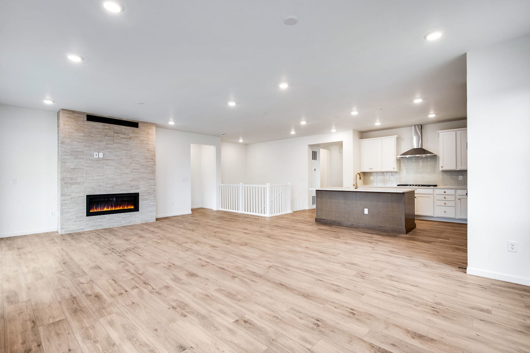 A spacious and modern open-concept living space with a fireplace, hardwood floors, and a kitchen with white cabinets and a central island.