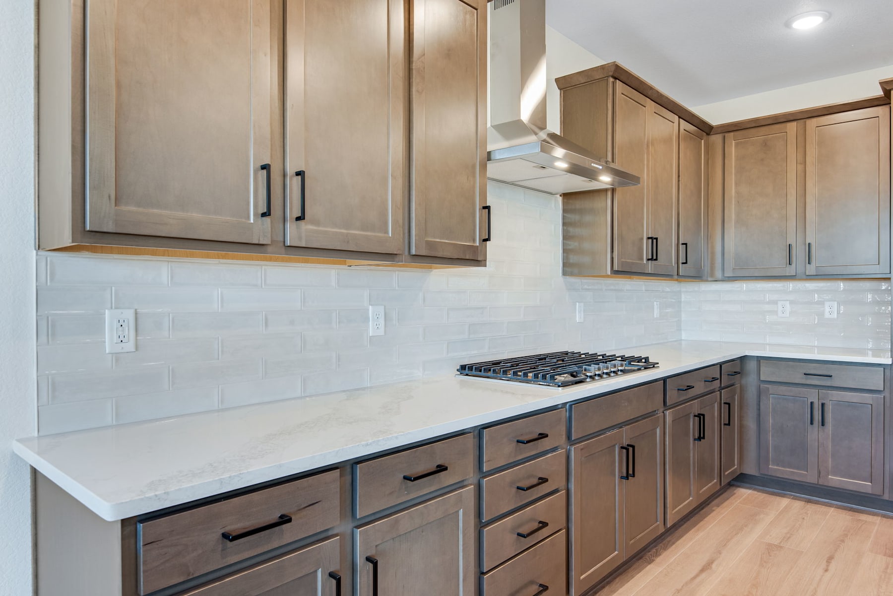 A modern kitchen with light-colored wooden cabinets, a gas stove, and a white countertop.