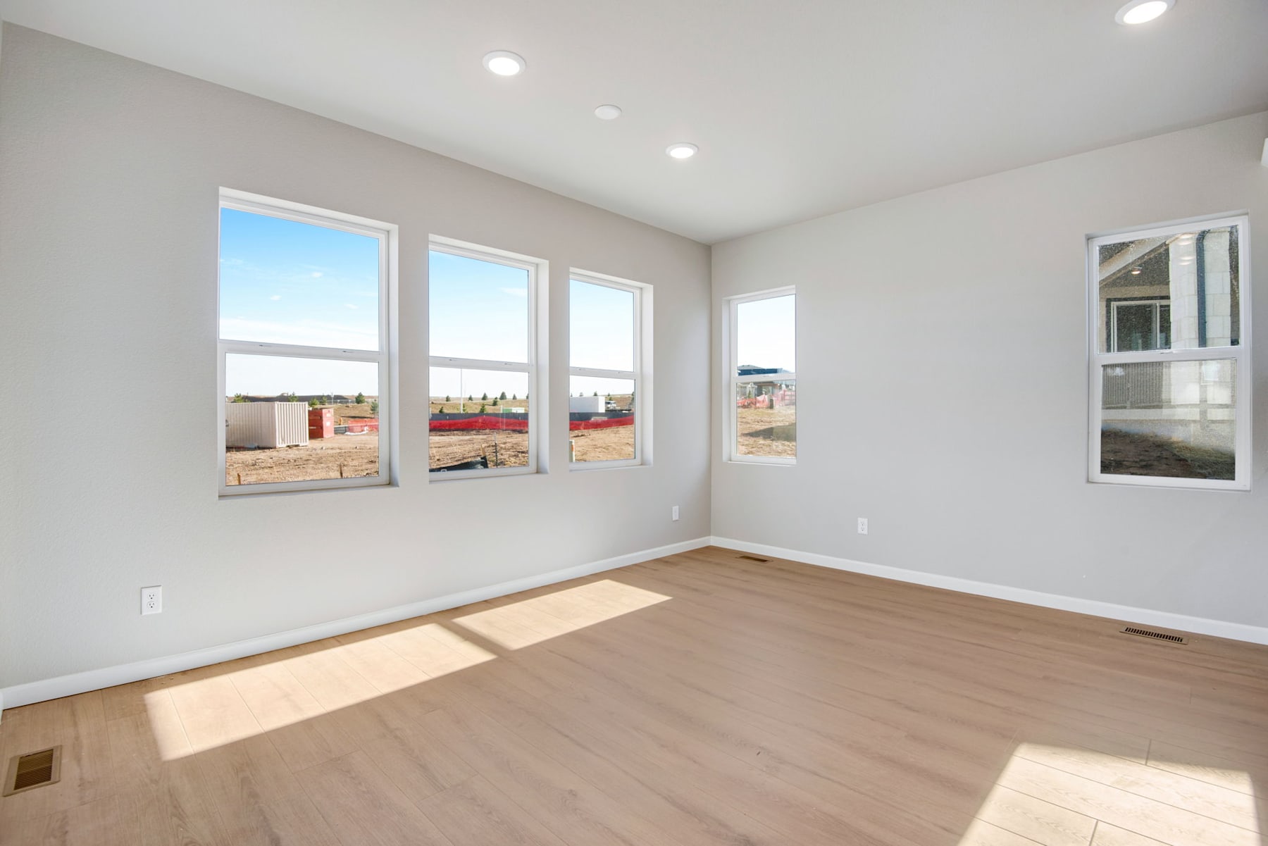 A bright and spacious room with large windows, hardwood floors, and recessed lighting, providing a view of the exterior surroundings.