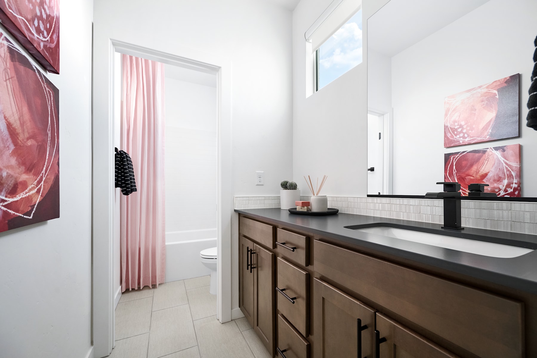 A modern bathroom with a dark wooden vanity, white tile walls, and large pink artwork hanging on the walls, creating a stylish and cohesive design.