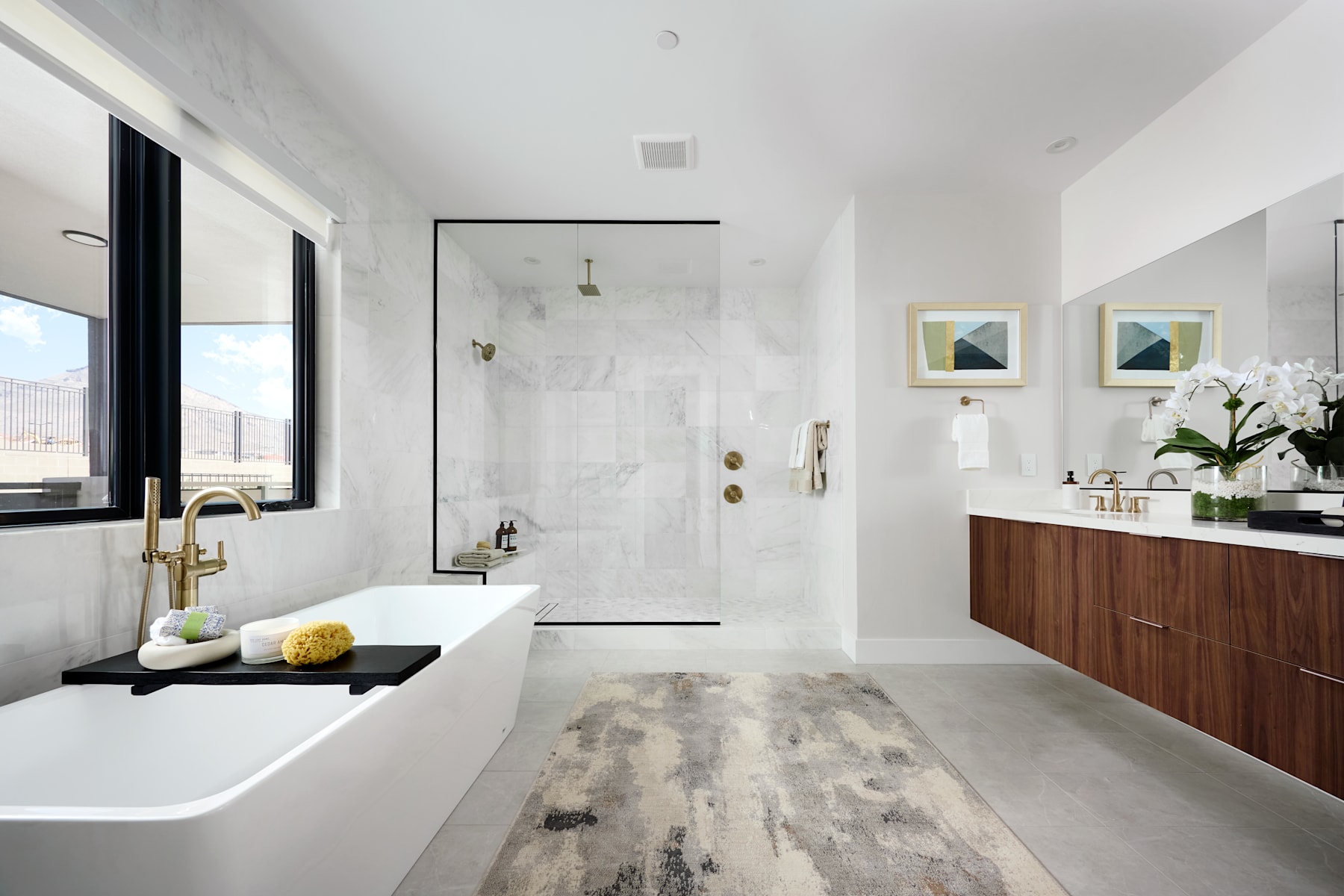 A modern, minimalist bathroom with a large freestanding bathtub, a wooden vanity, and framed artwork on the walls, overlooking a cityscape through the window.