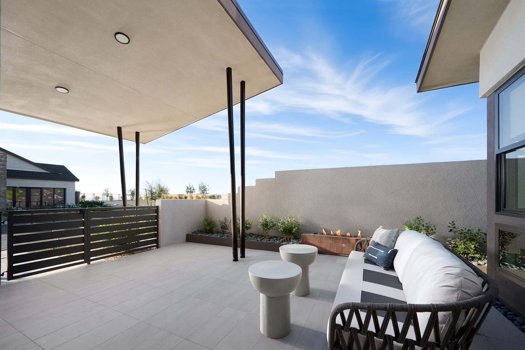 A modern outdoor patio with a covered seating area, surrounded by a low fence and featuring a clear blue sky in the background.