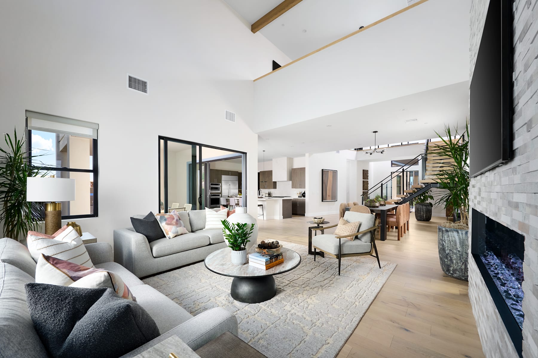 A spacious and modern living room with a cozy seating area, a fireplace, and an open-concept design that extends into the kitchen and dining area.
