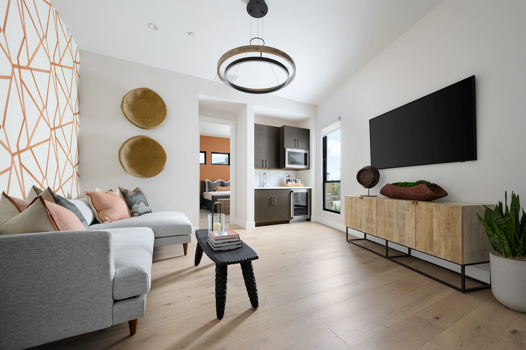 A modern and minimalist living room with a gray sofa, wooden media console, and decorative wall accents, creating a cozy and stylish atmosphere.