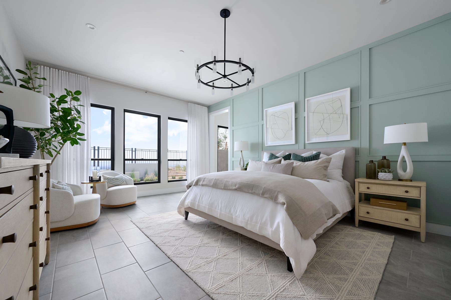 A spacious and modern bedroom with a large bed, neutral-toned decor, and a chandelier overhead, surrounded by large windows providing ample natural light.