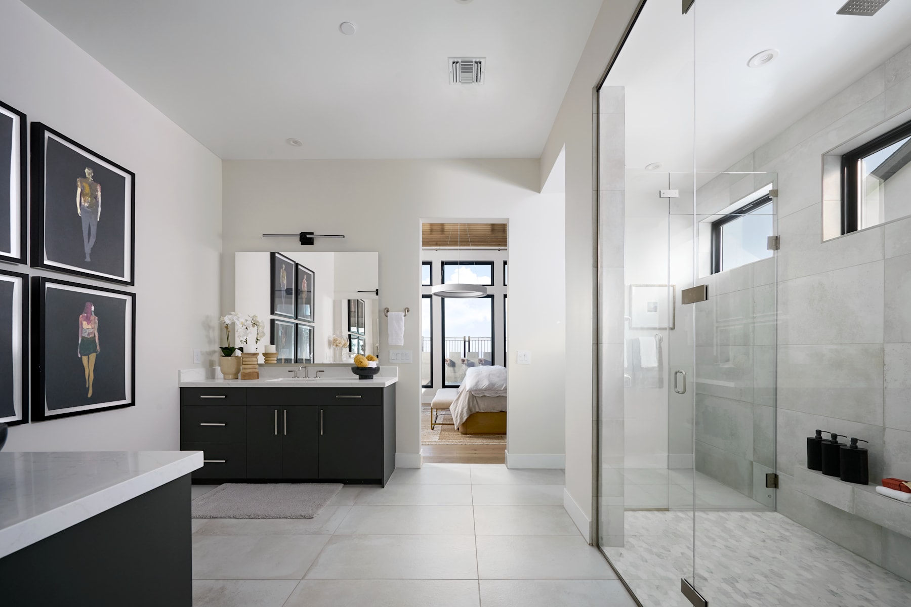 A modern, minimalist bathroom with a black vanity, framed artwork, and a glass-enclosed shower visible in the background.