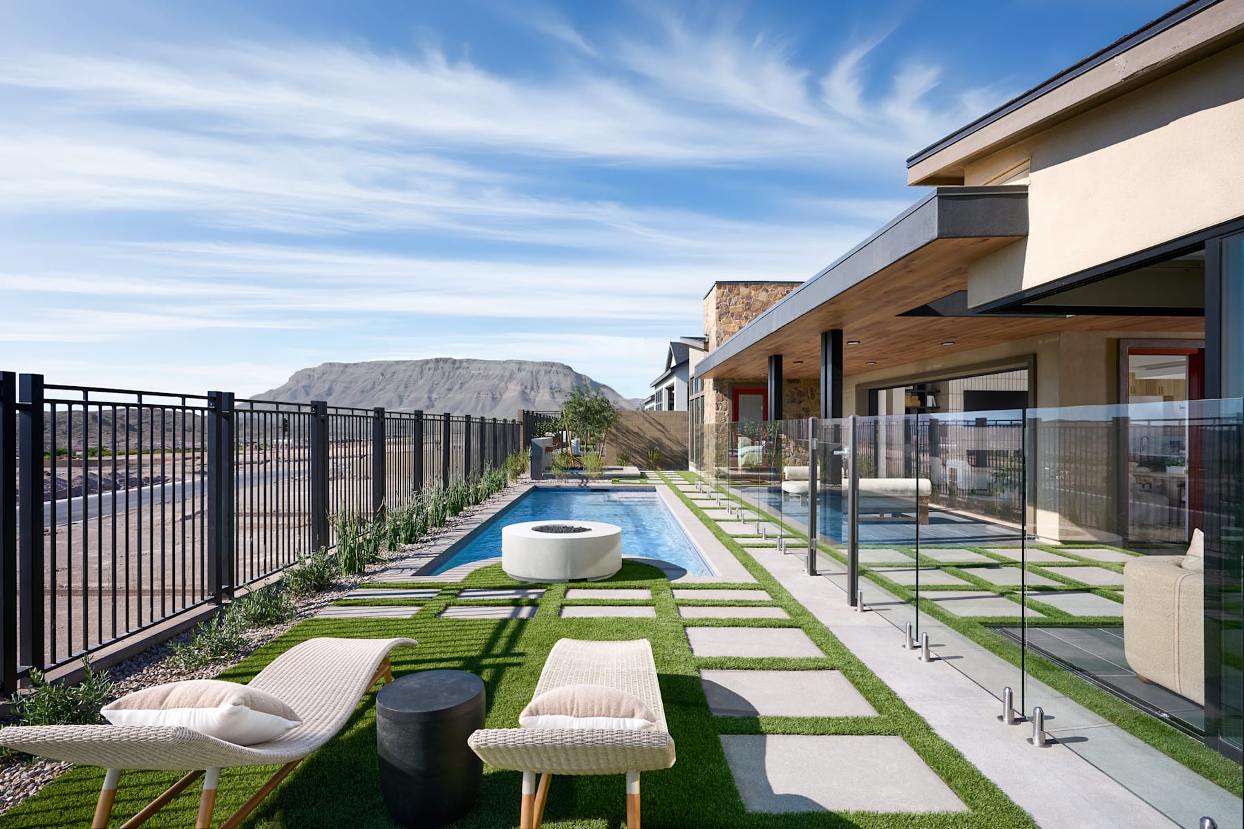 A modern outdoor patio with a pool, surrounded by a glass fence, with a mountainous landscape visible in the background.
