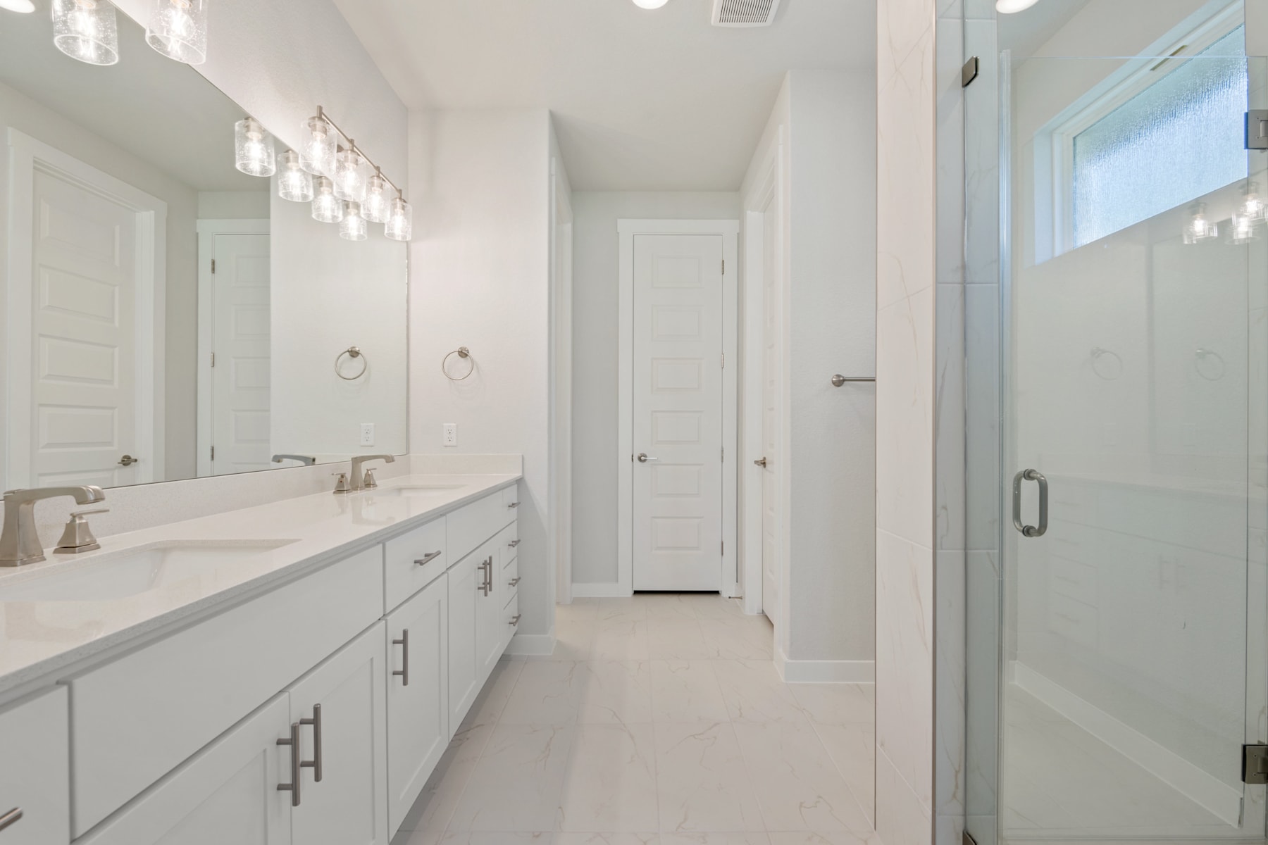 A bright and spacious bathroom with a long vanity, double sinks, and a glass-enclosed shower, all in a clean, modern design.