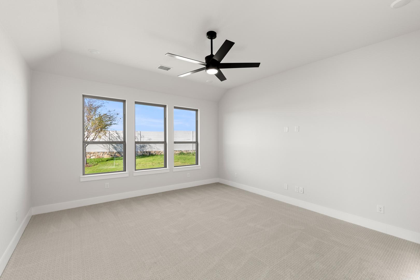 A spacious, well-lit room with a ceiling fan and large windows overlooking a grassy outdoor area.