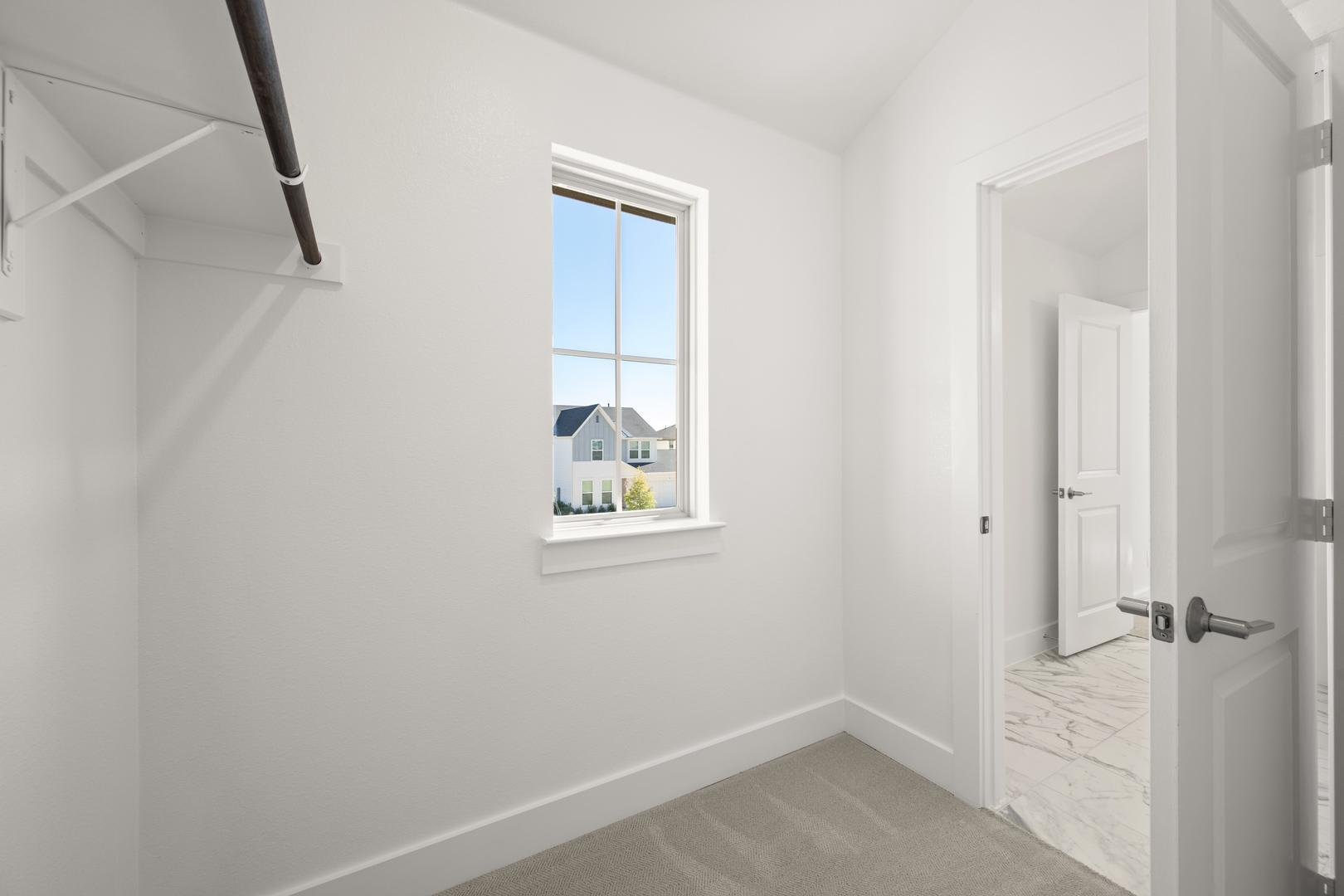 A bright, minimalist hallway with a window overlooking a residential neighborhood in the background.