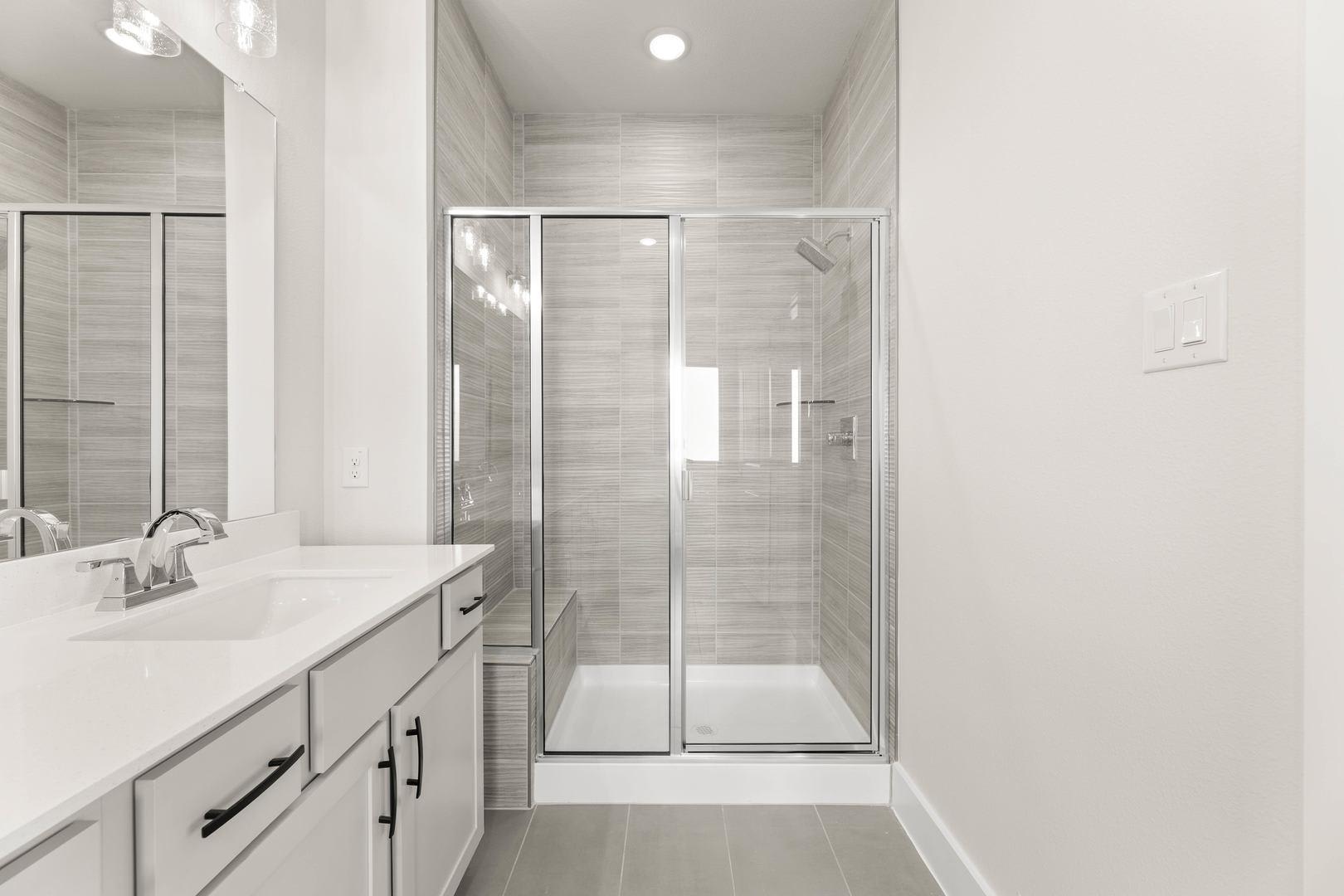 A modern, minimalist bathroom with a white vanity, a large mirror, and a glass-enclosed shower area, all set against a neutral color palette.