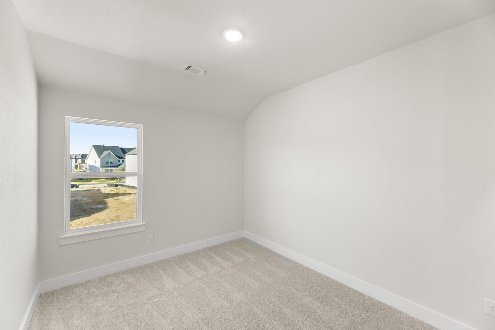 A bright, empty room with a window overlooking a residential neighborhood in the background.