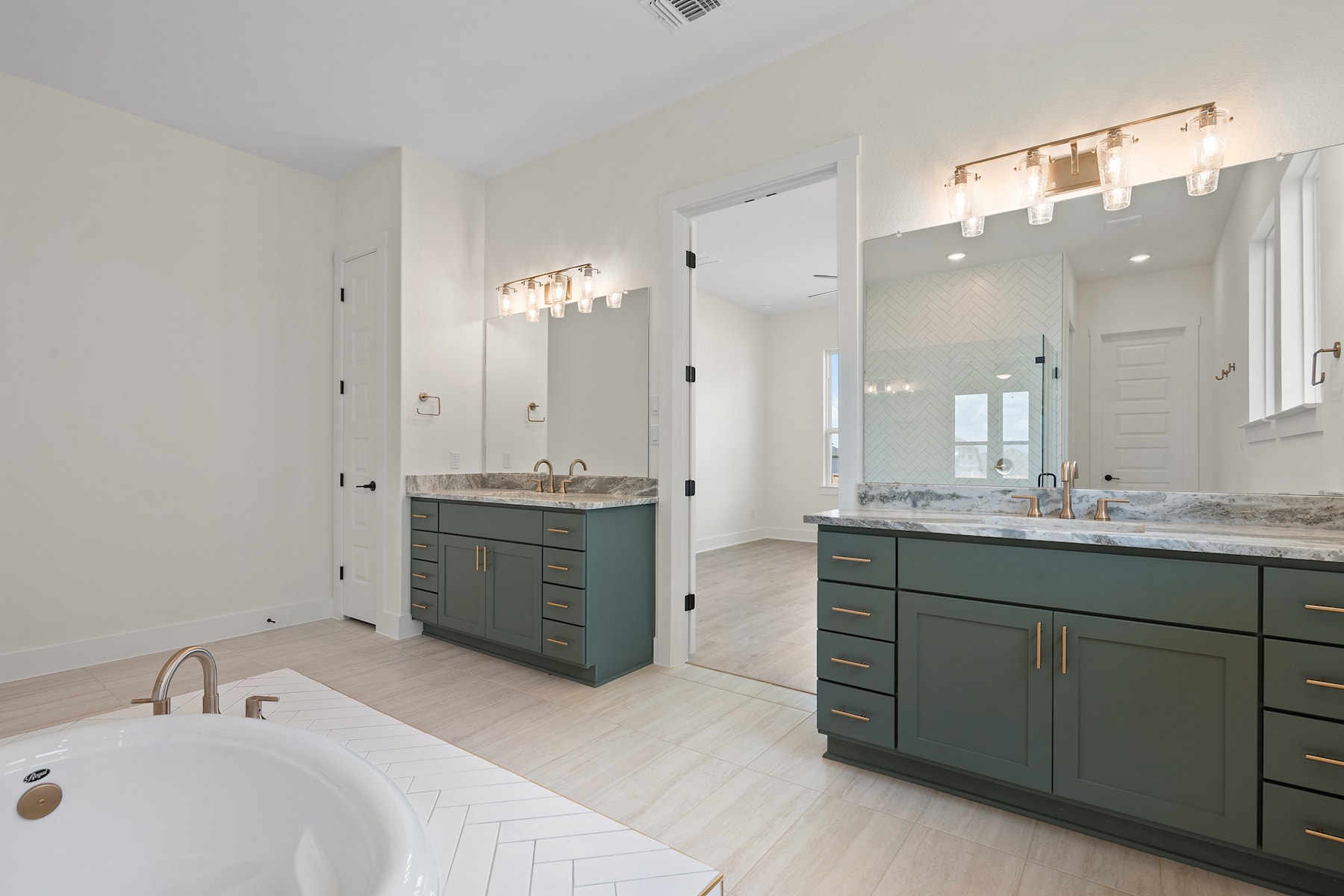 A spacious and modern bathroom with a white tiled floor, a large vanity with green cabinets, and a freestanding bathtub in the foreground.
