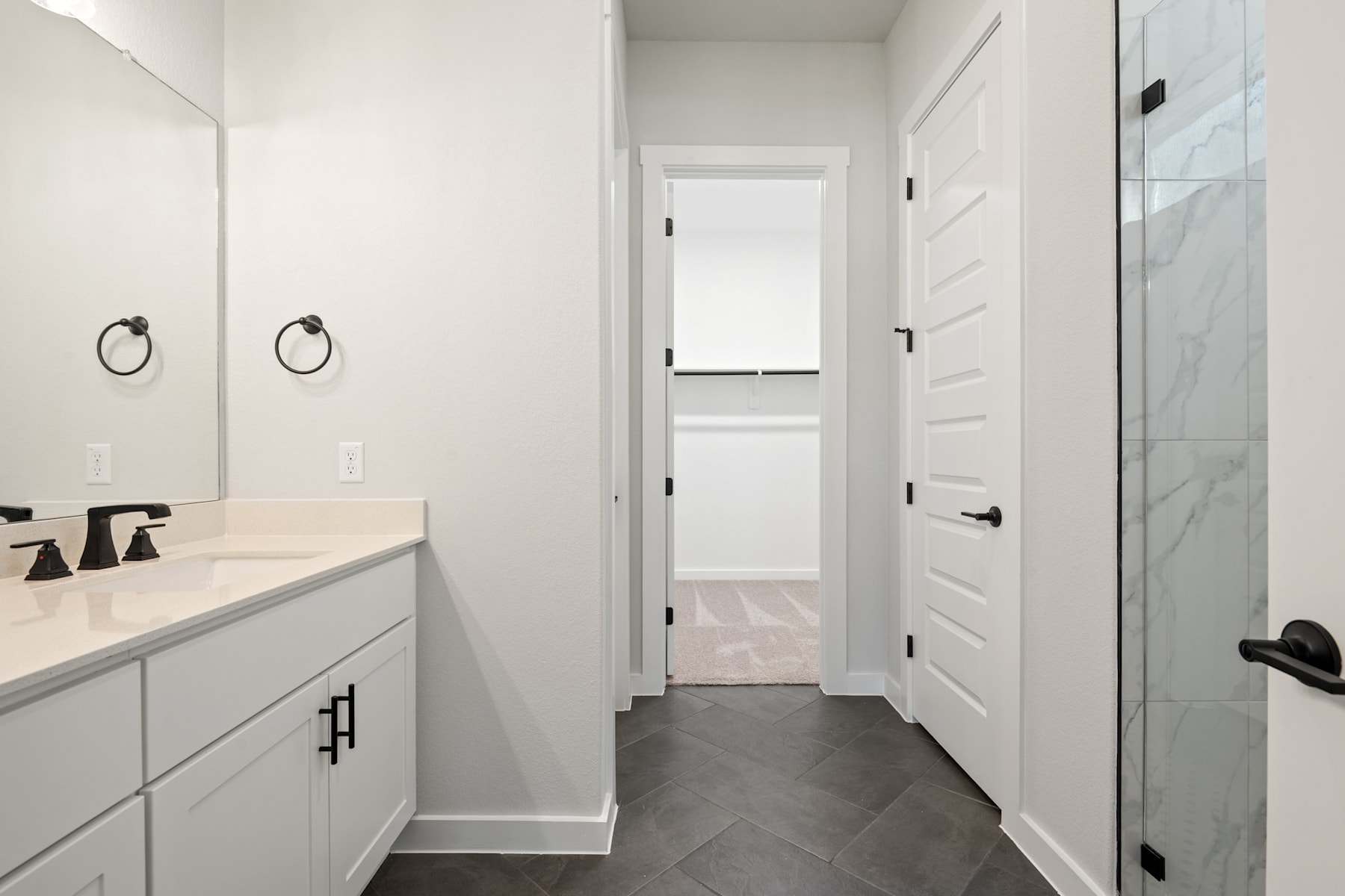A modern, minimalist bathroom with a vanity, mirrors, and a doorway leading to another room.