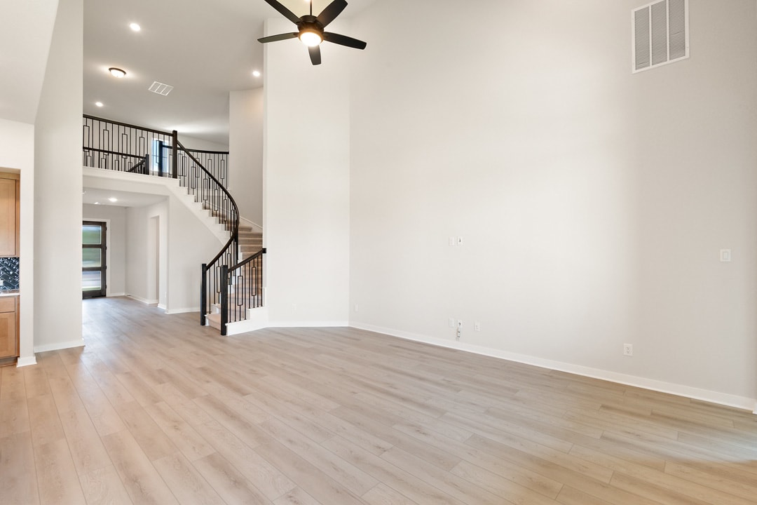 A spacious, open-concept room with a wooden floor, a ceiling fan, and a staircase leading to an upper level.