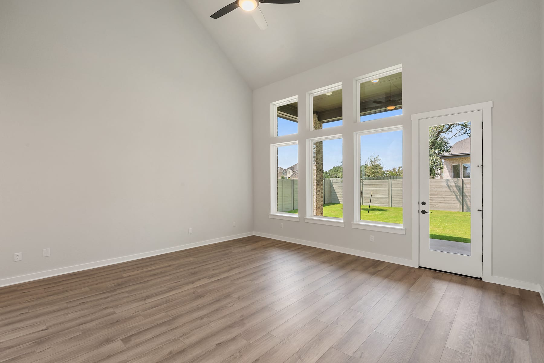 A bright and airy room with large windows overlooking a grassy outdoor area, featuring hardwood flooring and a white interior.