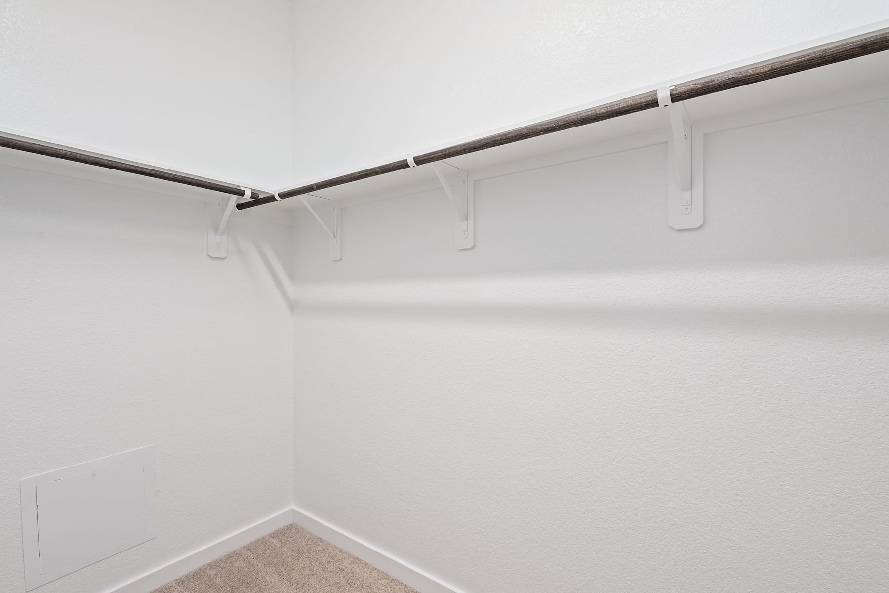 The image shows a simple, minimalist closet space with a metal rod and hangers suspended from the ceiling, creating a clean and organized storage solution against a plain white wall.