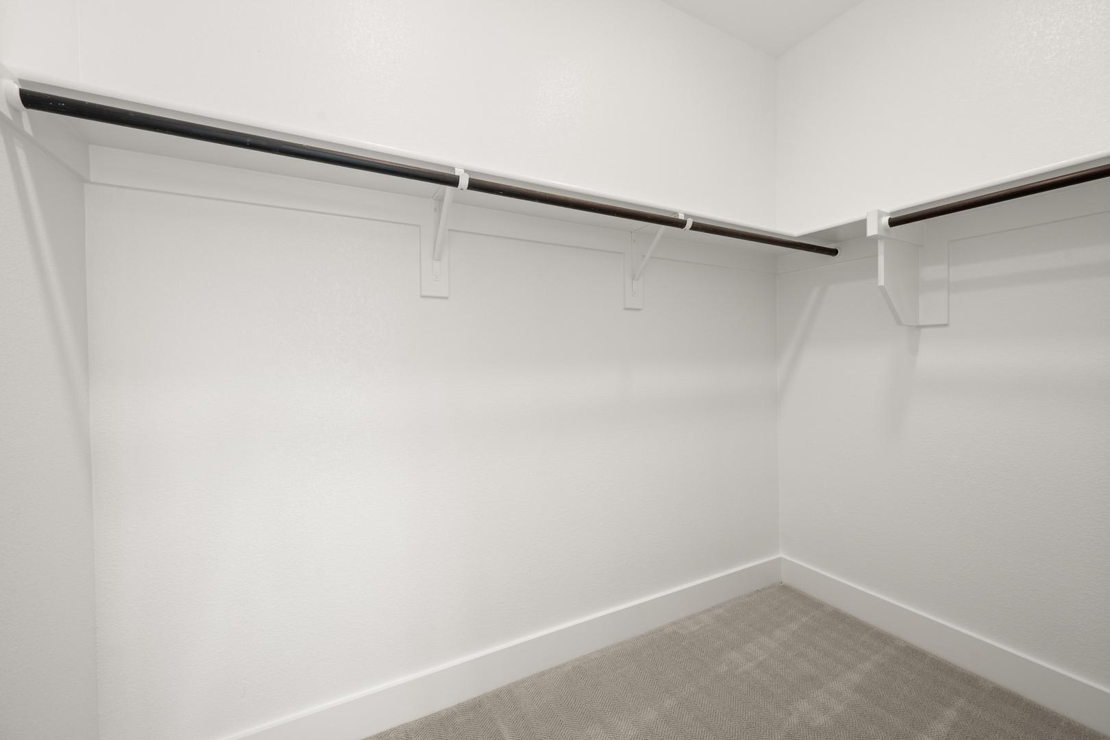 A simple, minimalist closet space with white walls and a metal hanging rod for storing clothes.