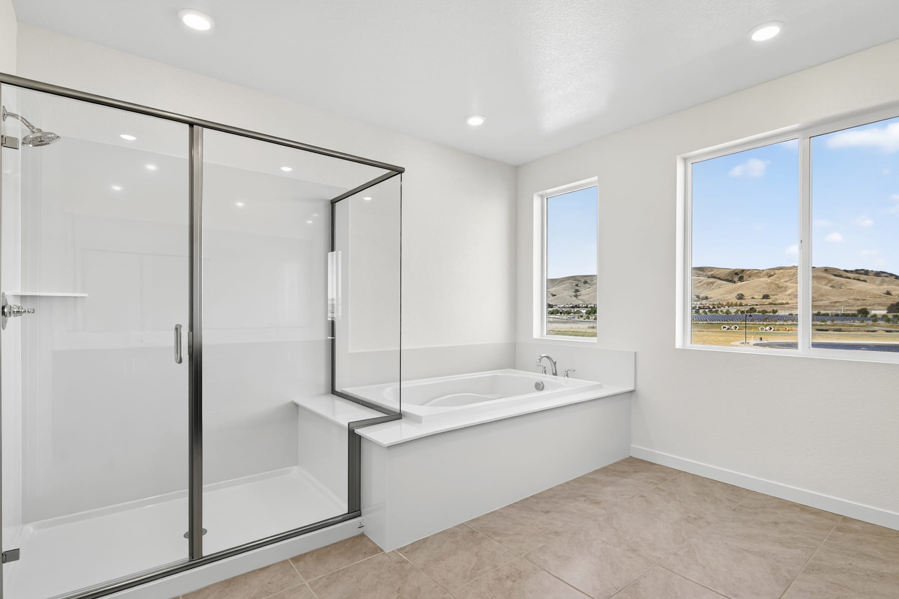 A modern, bright bathroom with a large bathtub, glass shower enclosure, and a scenic view of the surrounding landscape visible through the windows.