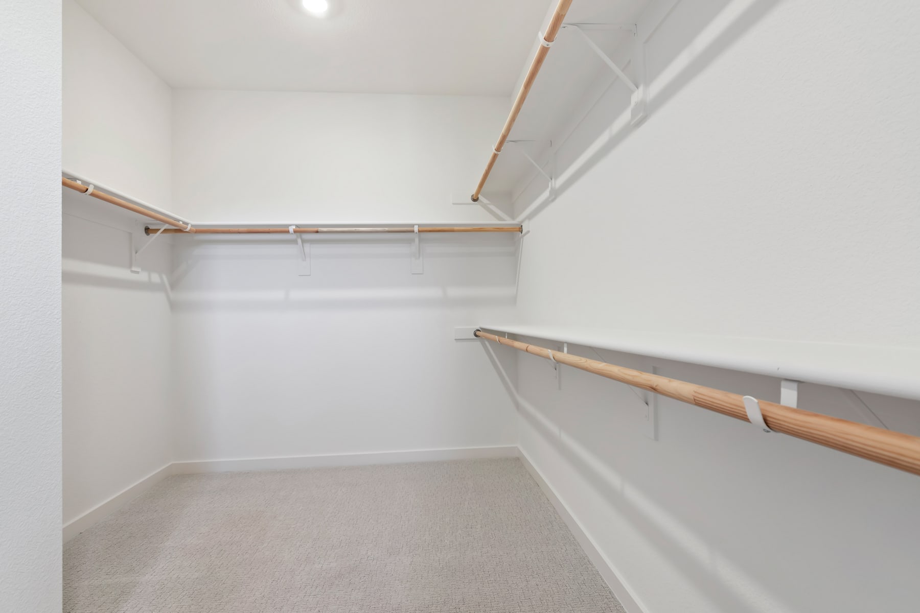 A spacious, well-lit closet with white walls, wooden shelves, and a metal hanging rod for storing clothes.