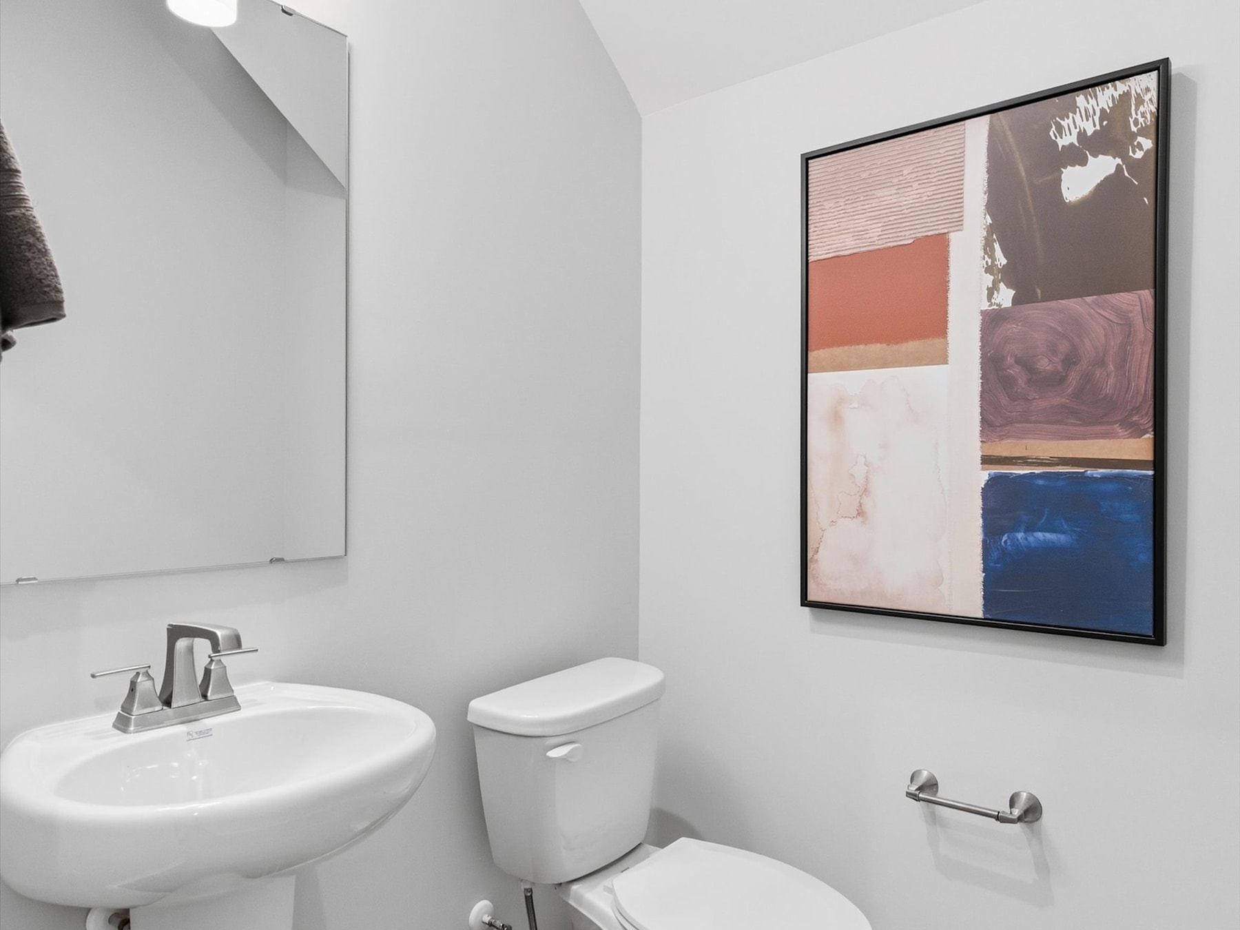 A modern bathroom with a white sink, toilet, and a framed abstract artwork on the wall.