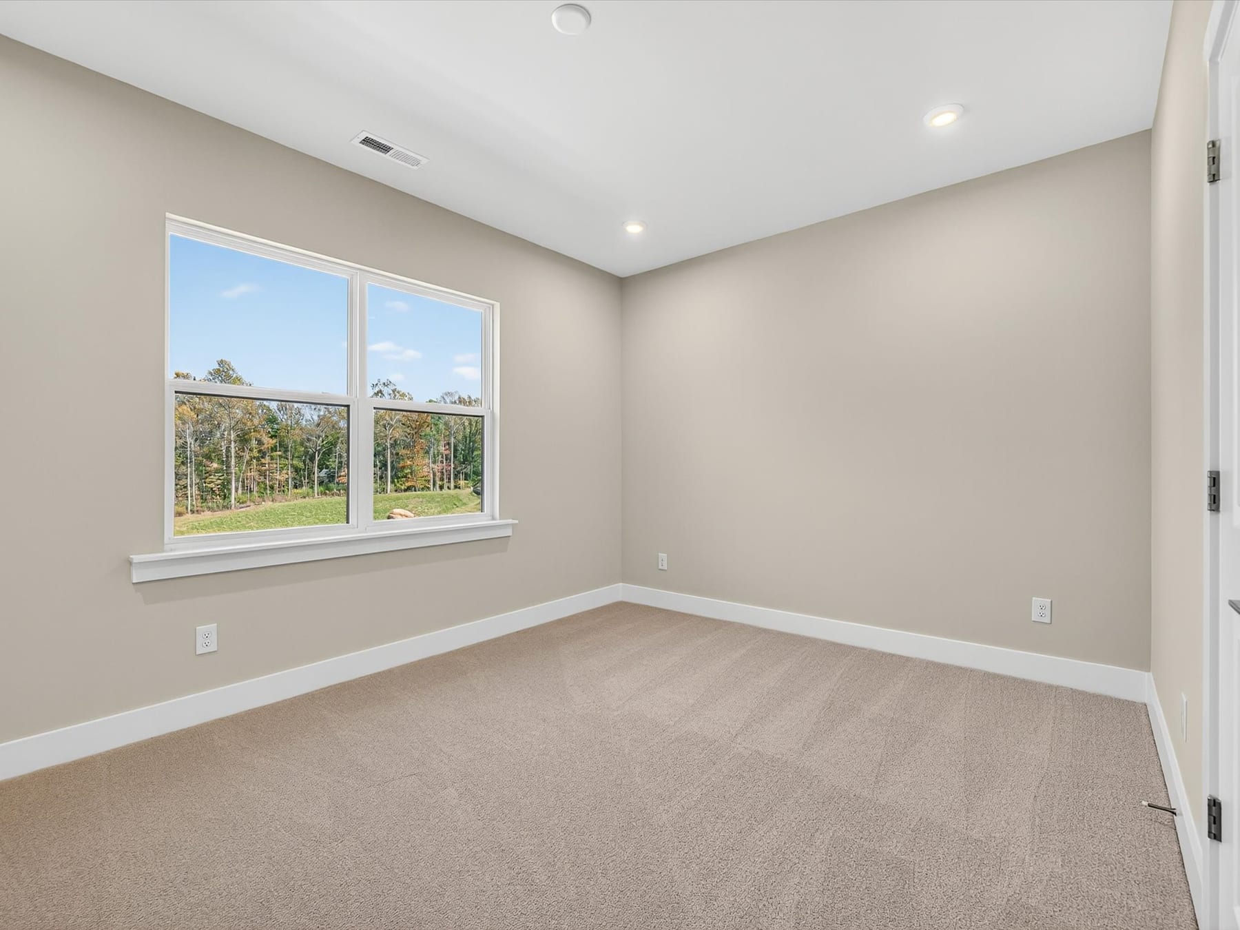 A spacious, well-lit room with large windows overlooking a scenic outdoor landscape, featuring a neutral-toned color scheme and plush carpeting.