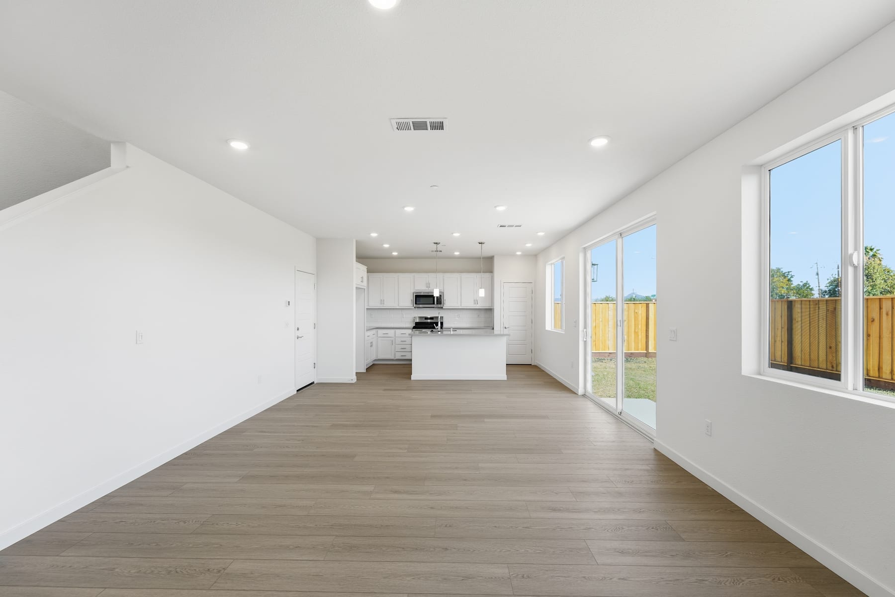 A spacious, modern interior with a minimalist design, featuring a kitchen area, hardwood flooring, and large windows providing ample natural light.