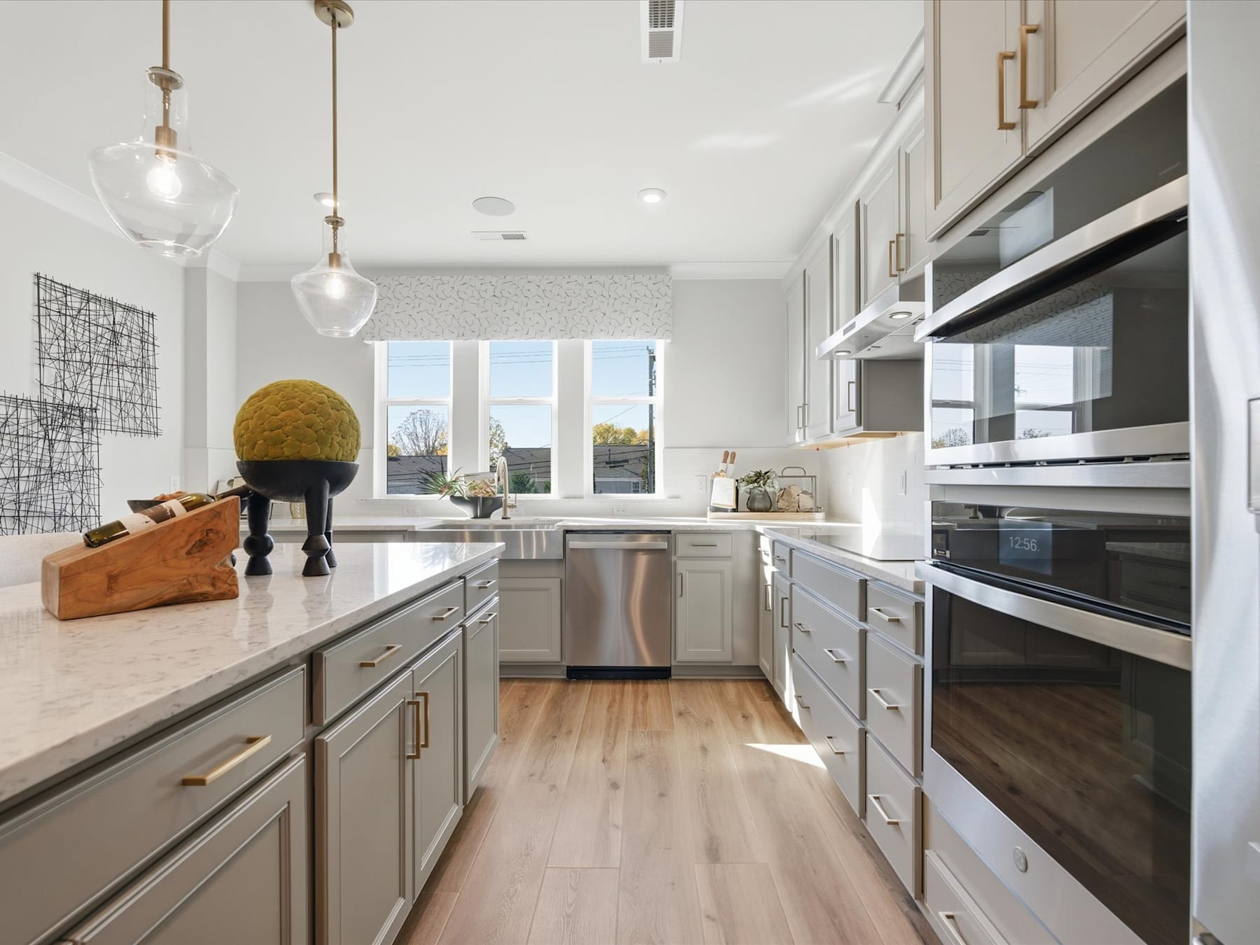 A modern, well-lit kitchen with sleek gray cabinets, stainless steel appliances, and a wooden floor. In the foreground, there is a large, round, yellow object that appears to be a decorative element.