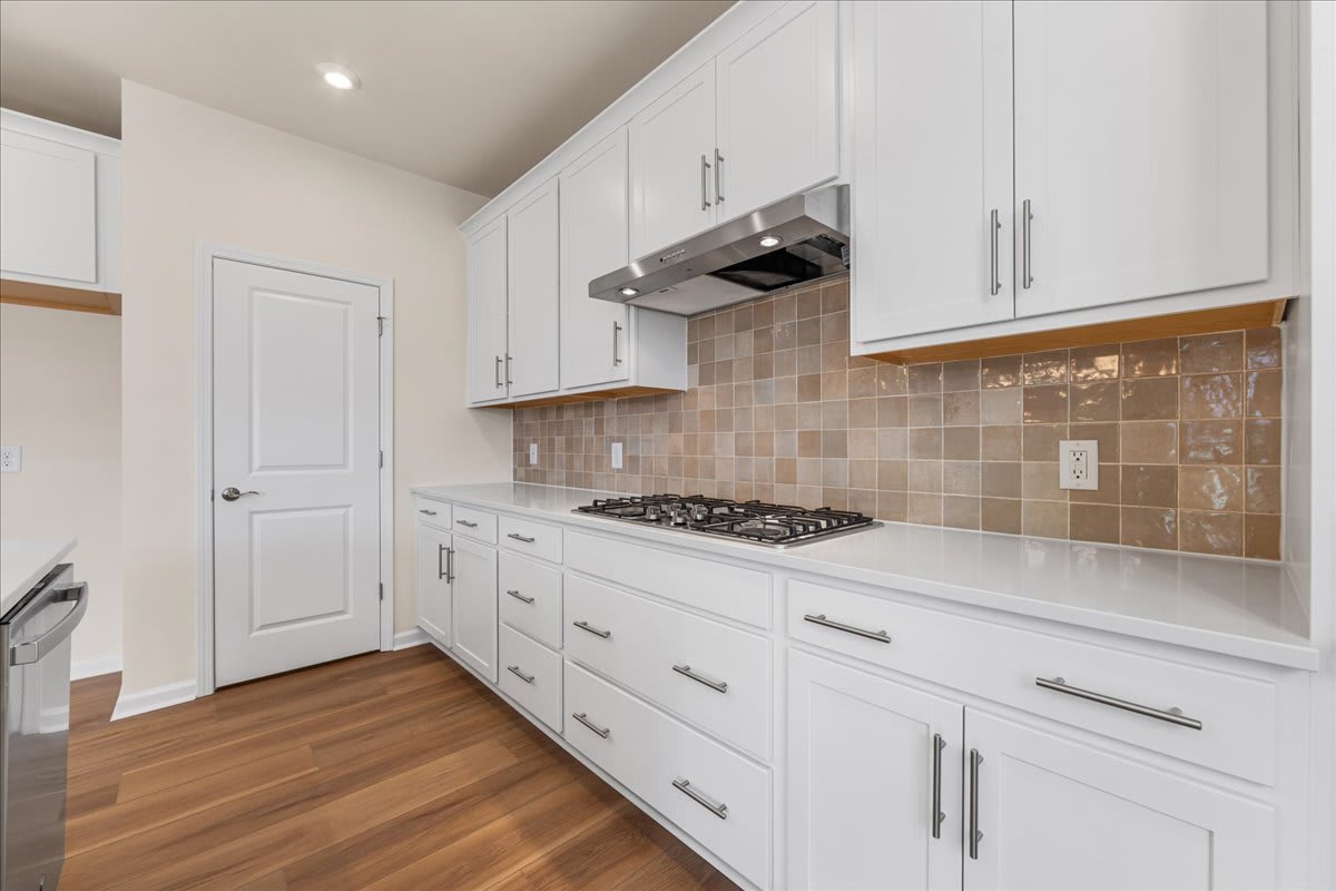 A modern, well-equipped kitchen with white cabinets, a tiled backsplash, and hardwood flooring.