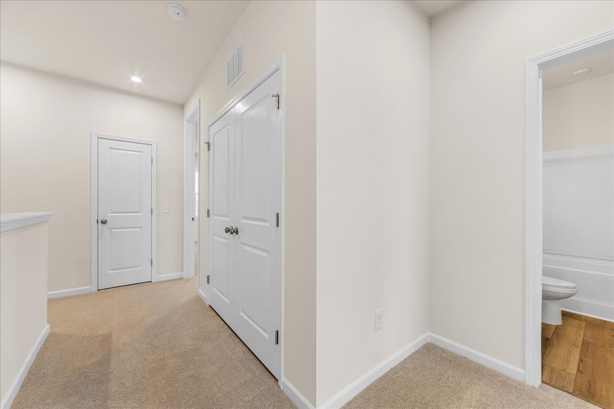 A bright, minimalist hallway with white walls, wooden floors, and a closed door leading to another room.