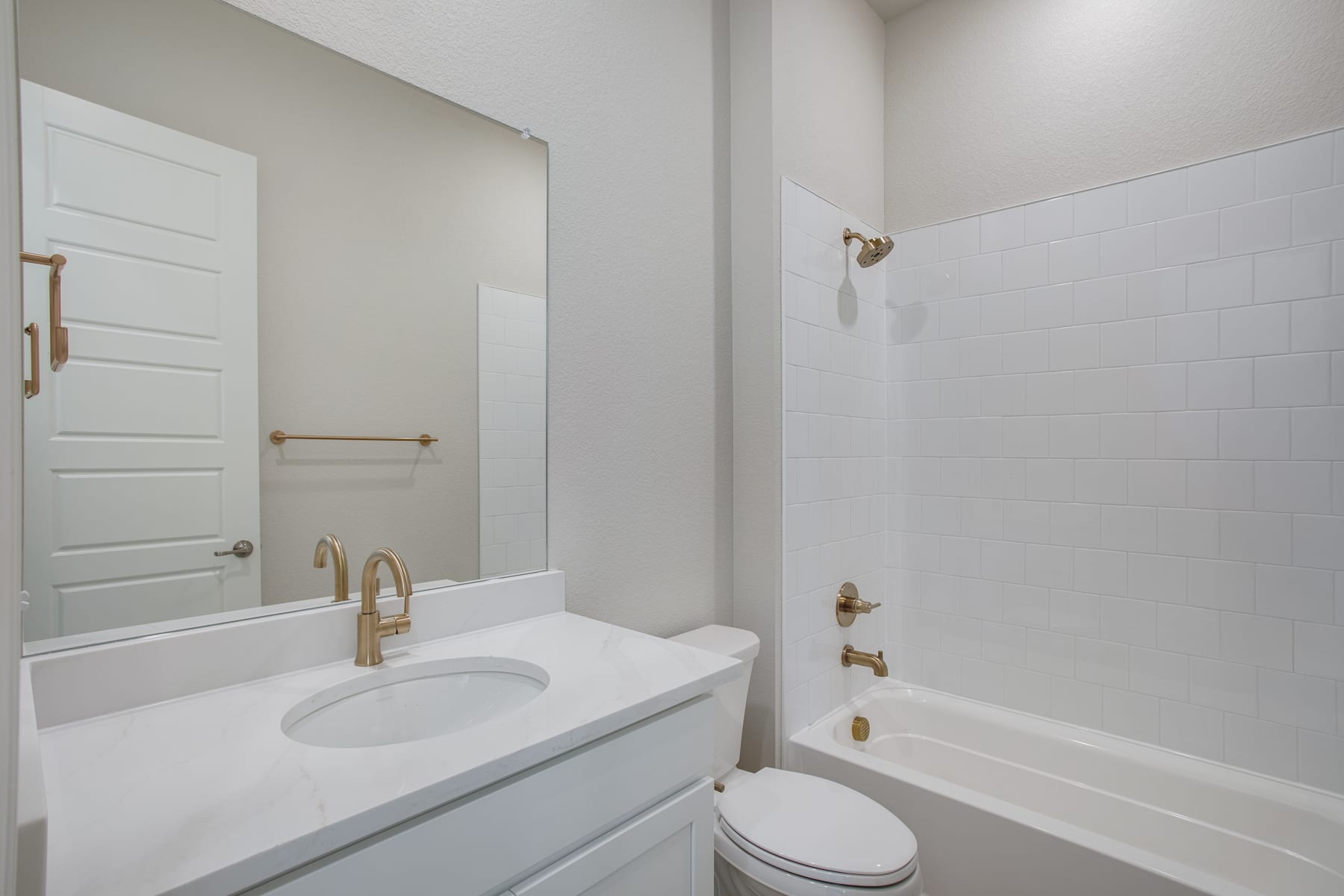 A modern, minimalist bathroom with a white vanity, a toilet, and a bathtub surrounded by white walls and a mirror.