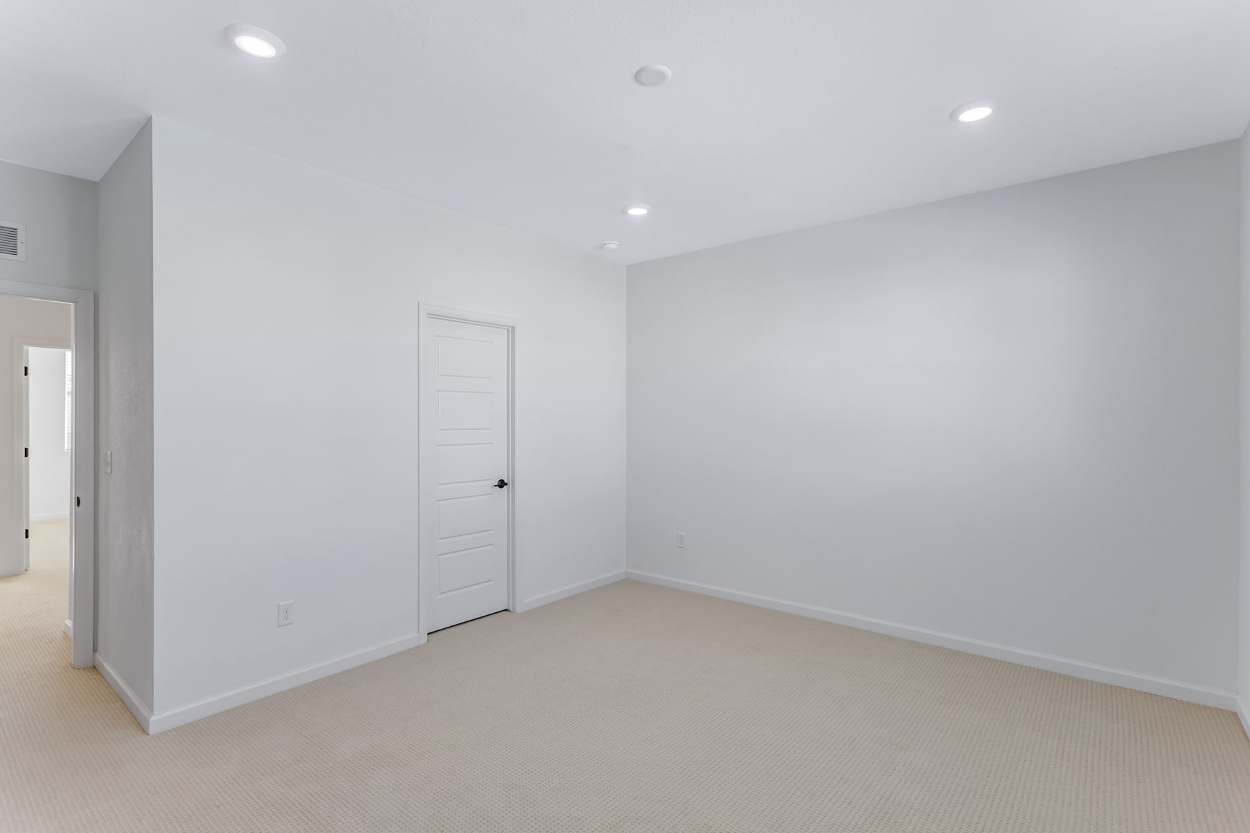 A bright, minimalist room with white walls, a white door, and recessed lighting fixtures on the ceiling.