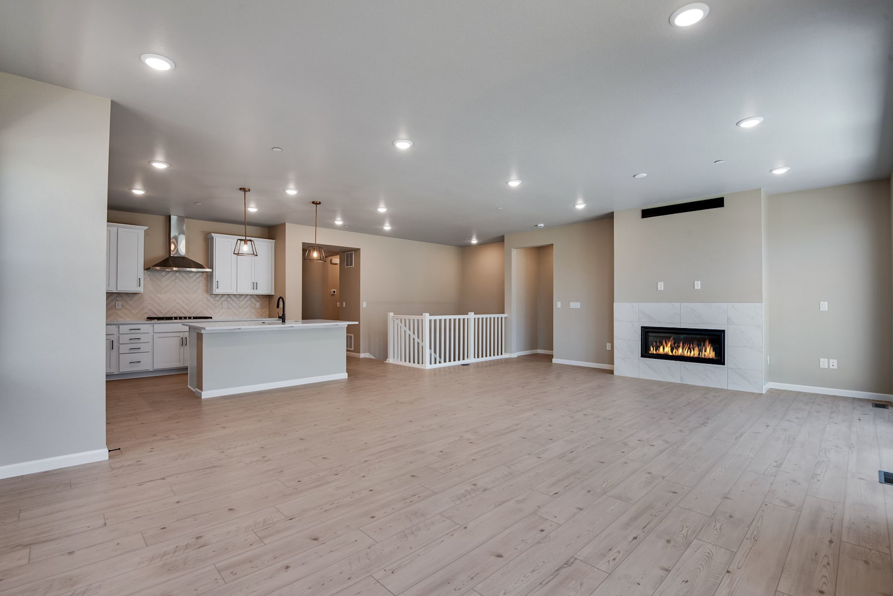 A spacious and modern open-plan living area with a kitchen, fireplace, and hardwood flooring.