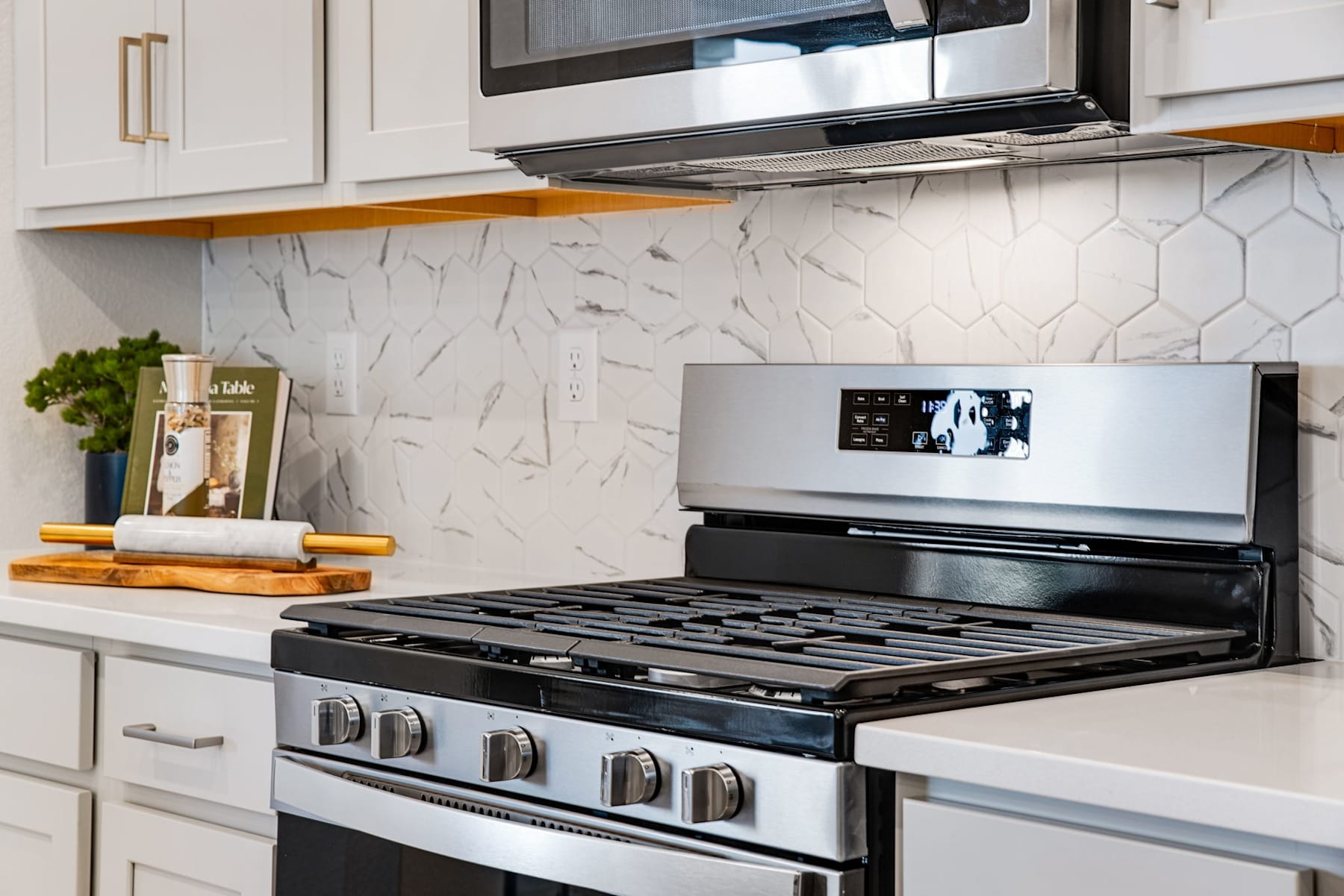 A modern kitchen with white cabinets, a marble backsplash, and a stainless steel gas stove with various cooking utensils and decor items on the countertop.