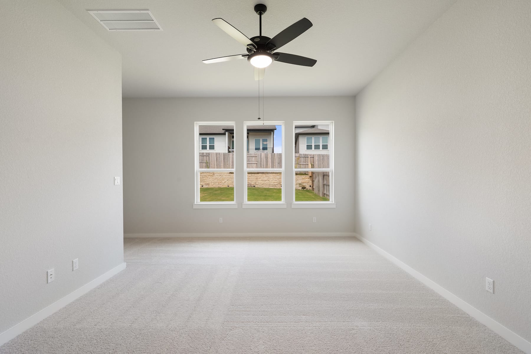 A spacious, well-lit room with a ceiling fan and large windows overlooking a grassy outdoor area.