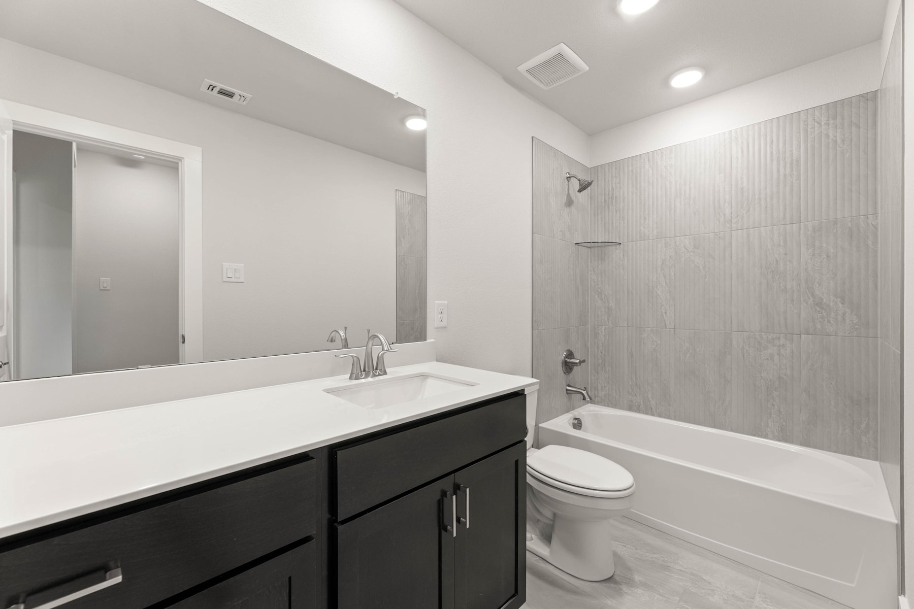 A modern bathroom with a black vanity, white countertop, and a large mirror on the wall. The room features a bathtub, shower, and toilet, all in a clean, minimalist design.