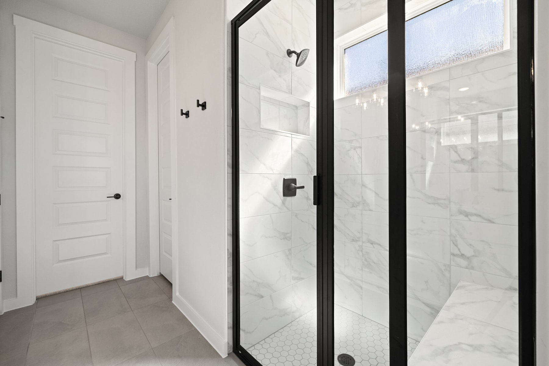 A modern, minimalist hallway with a white door, black-framed glass panels, and a marble-tiled floor.