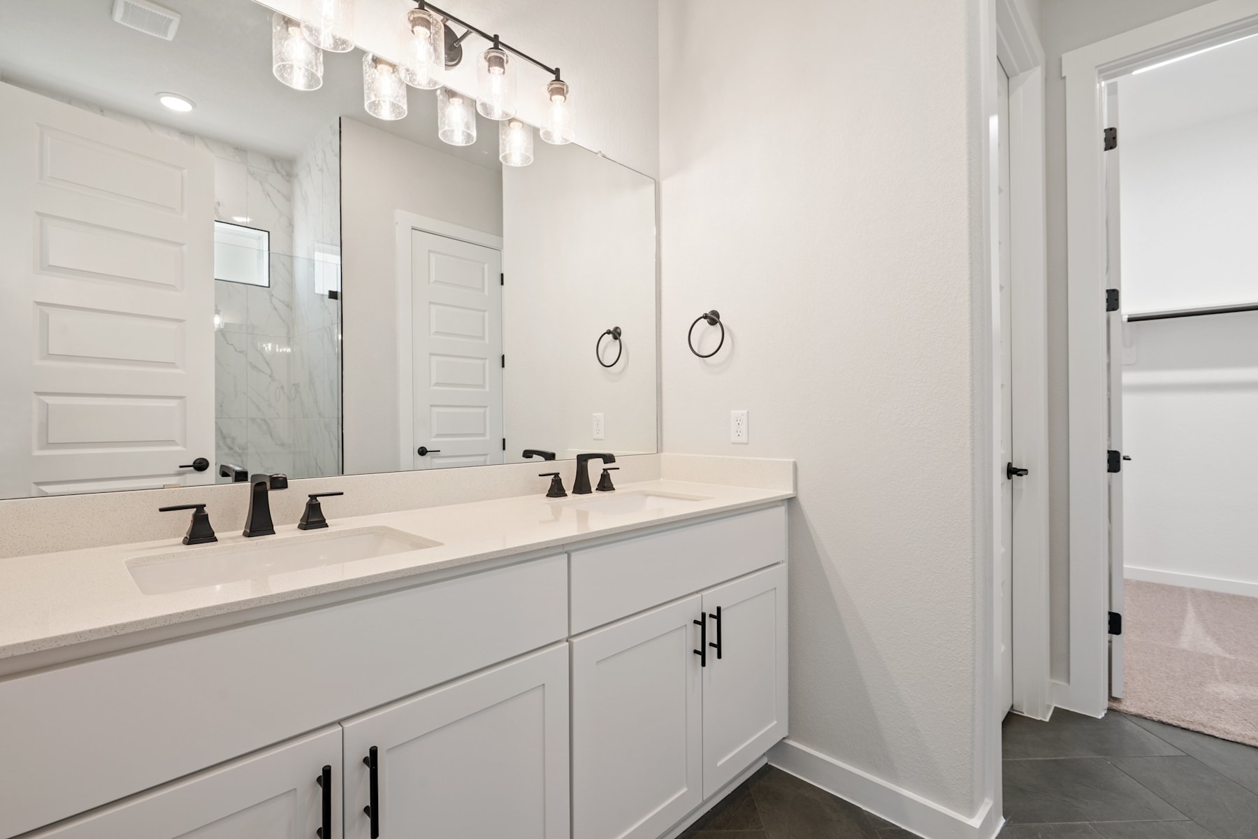 A modern and minimalist bathroom with a white vanity, double sinks, and a large mirror with a stylish light fixture above it.