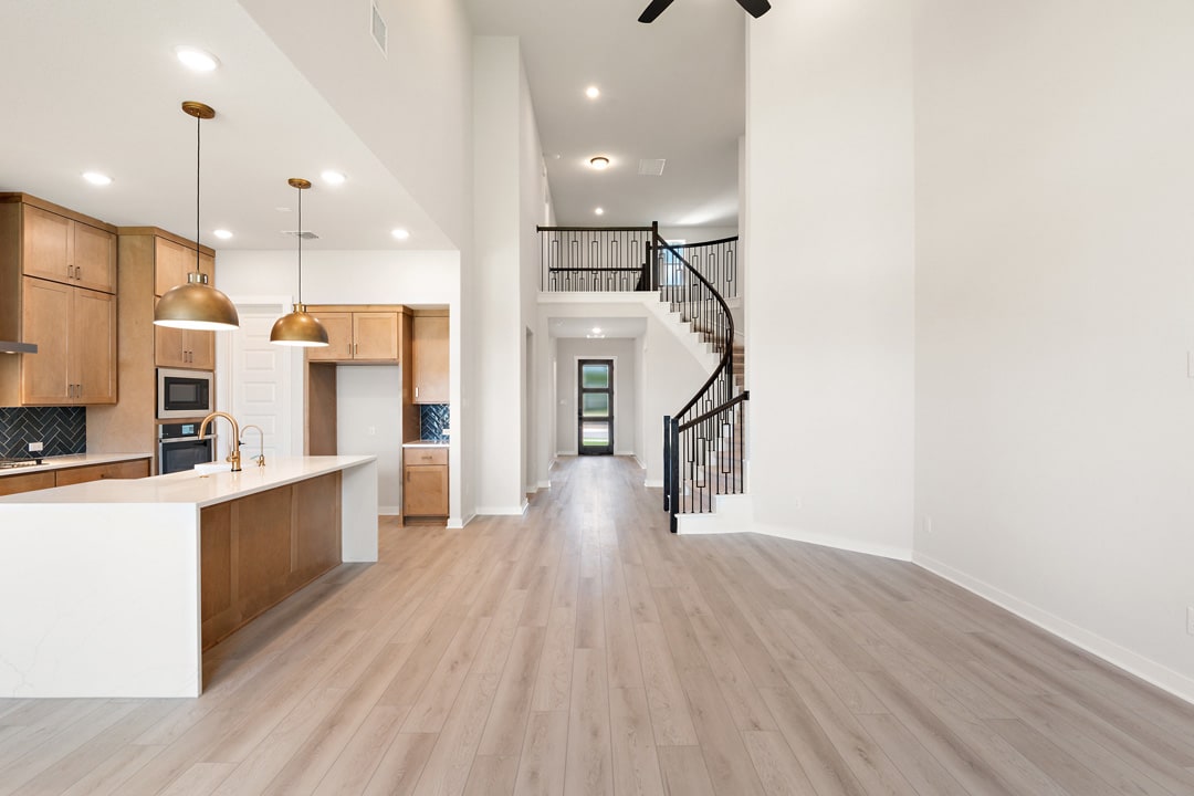 A modern, open-concept kitchen and living space with wooden cabinetry, pendant lighting, and a spiral staircase leading to an upper level.