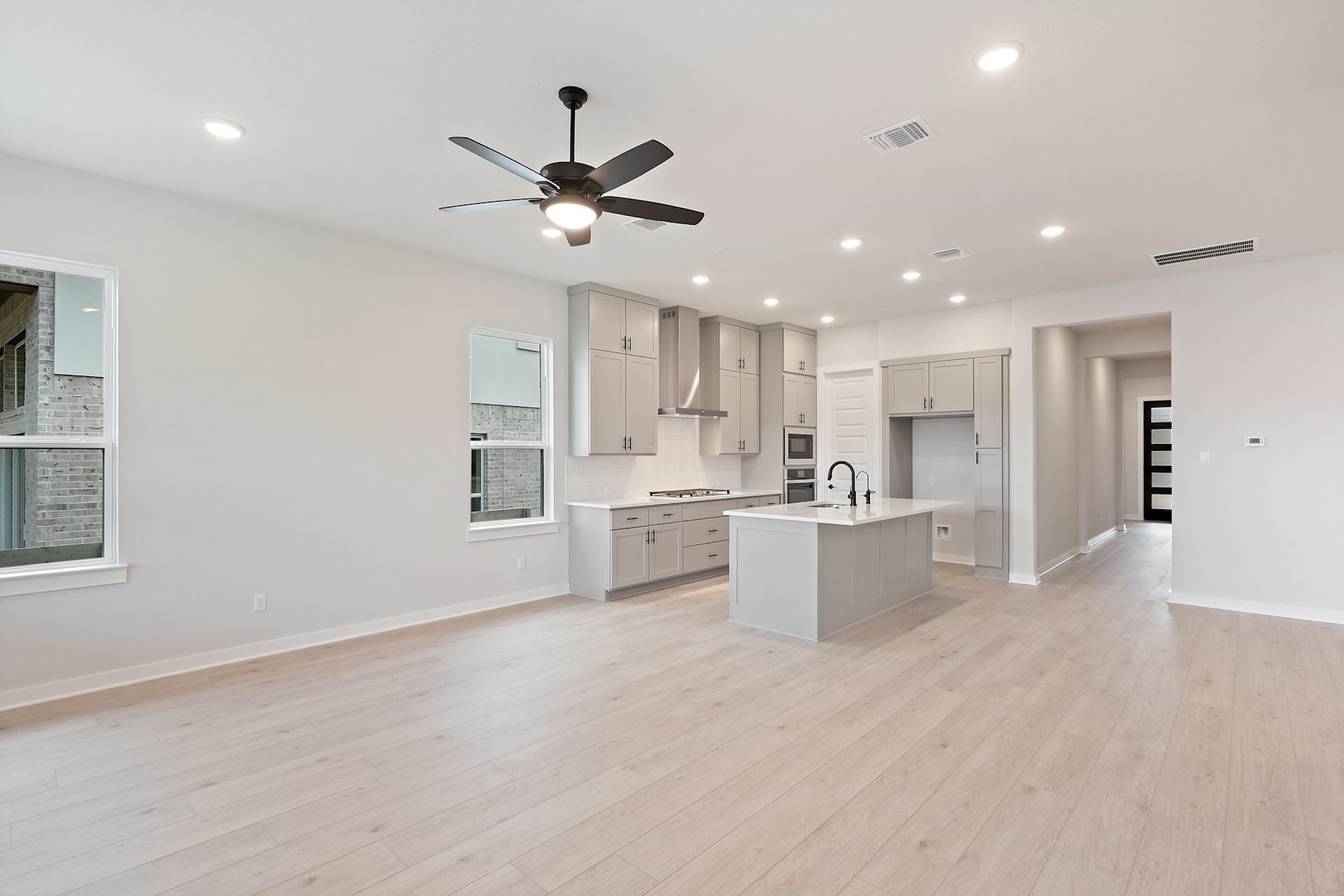 A modern, open-concept kitchen and living space with white cabinets, hardwood floors, and a ceiling fan.