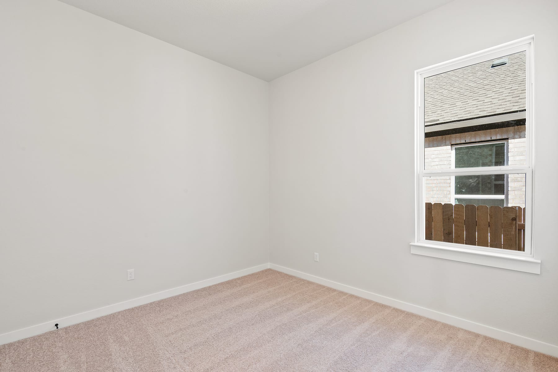 A simple, minimalist room with white walls, a wooden window frame, and a hardwood floor.