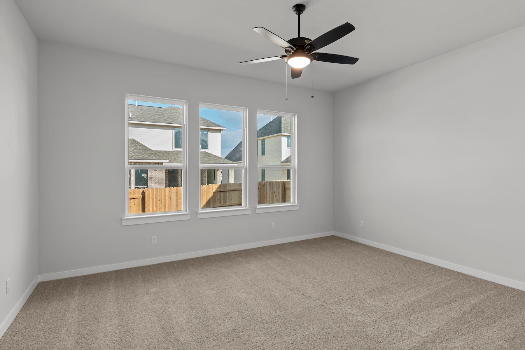 A spacious, well-lit room with a ceiling fan and large windows overlooking a residential area.